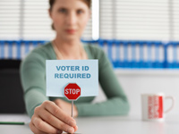 Voter ID Laws can restrict older voters, Woman in an office holding a little stop-sign and paper that reads Voter ID Required	