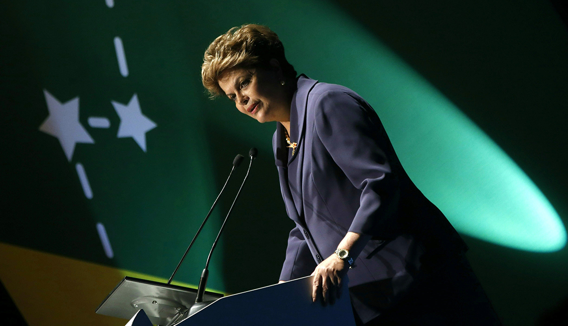 Dilma Rousseff waist length tilted making a speech with green background with white stars and dashes