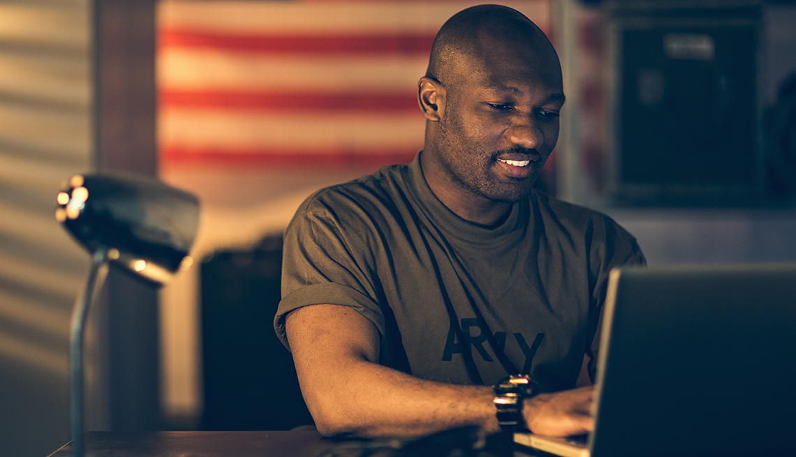 Hombre con camisa del ejército frente a una computadora en una oficina.