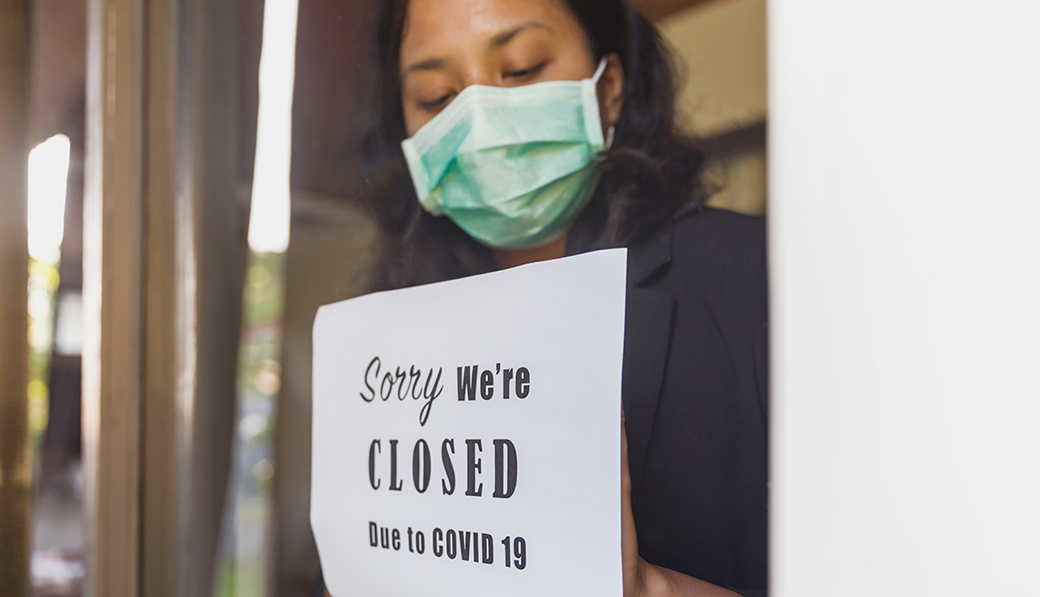 Una mujer muestra un anuncio en la ventana de un negocio que dice en inglés -cerrado debido al coronavirus-