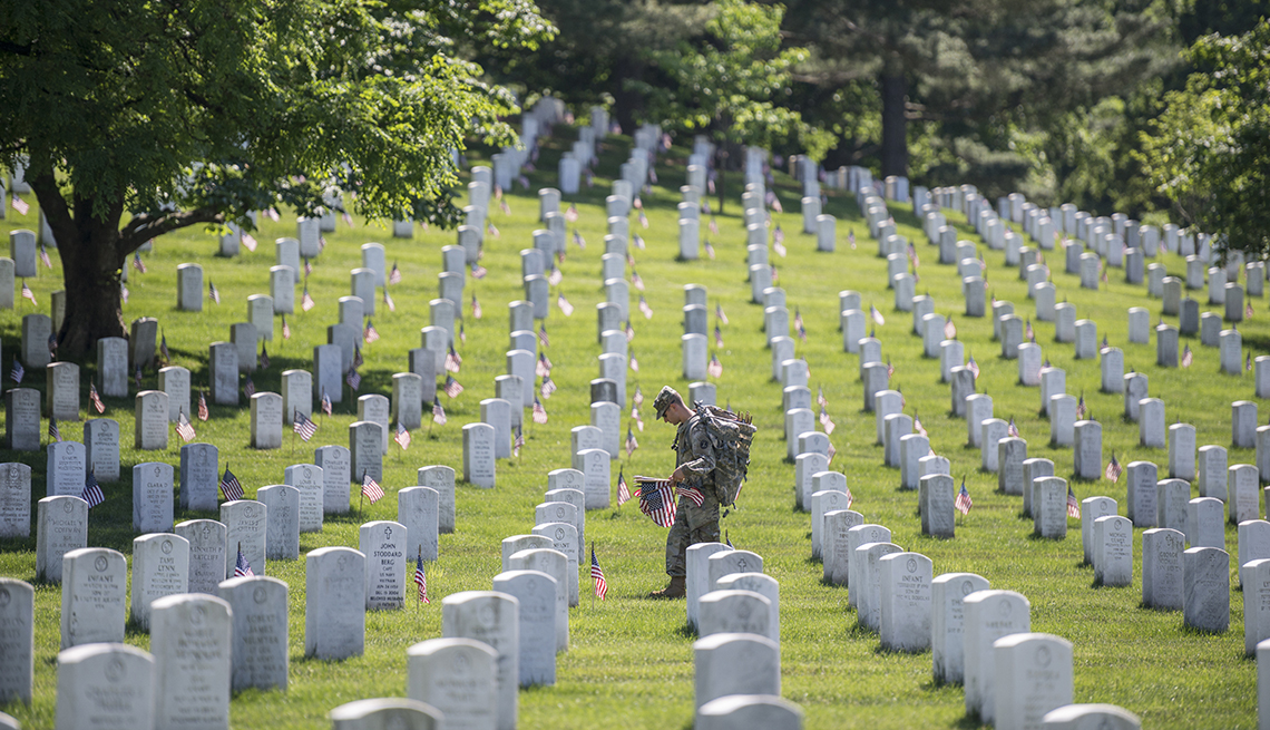 Un soldado pone banderas en las tumbas de un cementerio