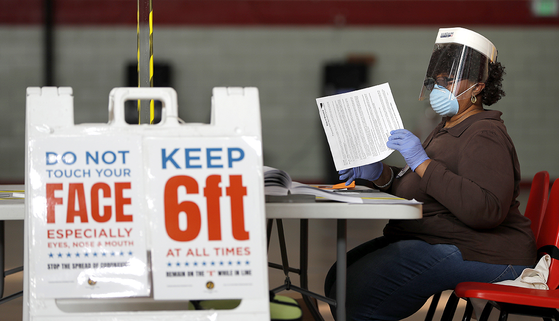 Mujer, protegida con una máscara, está sentada en un lugar de votación electoral