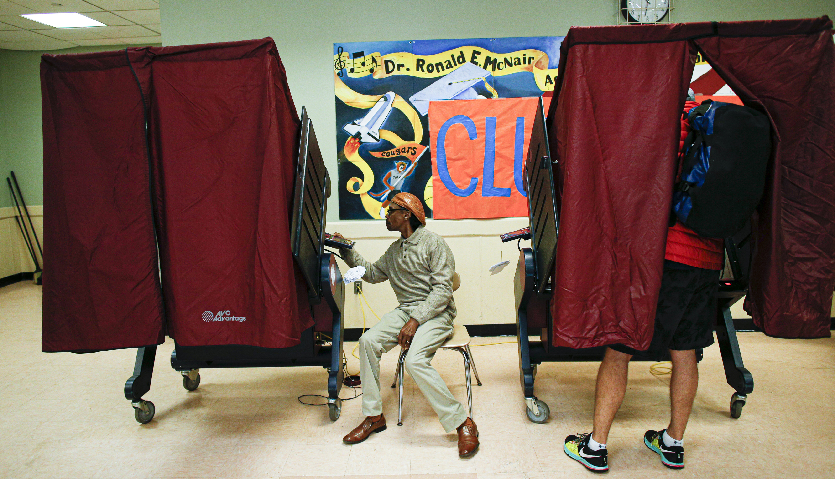 a man votes in a red-curtained polling booth at a school
