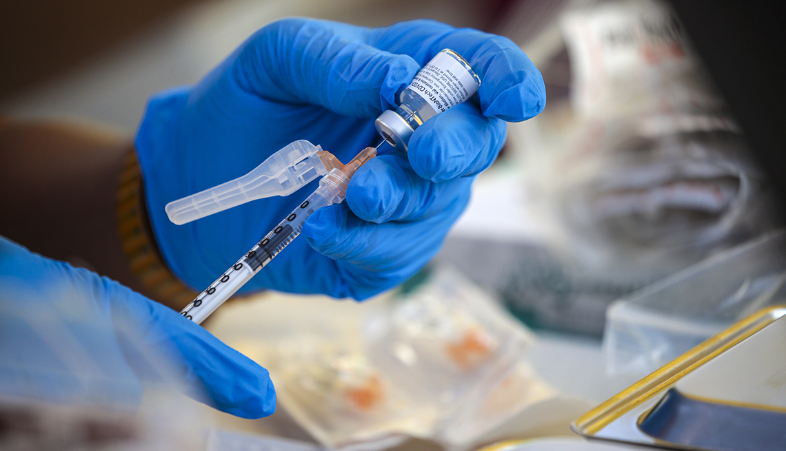 Manos de una persona con guantes mientras manipulan una vacuna de la COVID-19 en un centro de vacunación móvil en Los Ángeles