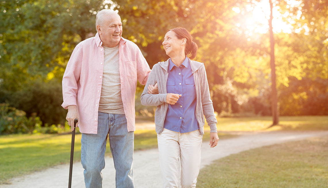 A man with a cane and his caregiver walking in a park