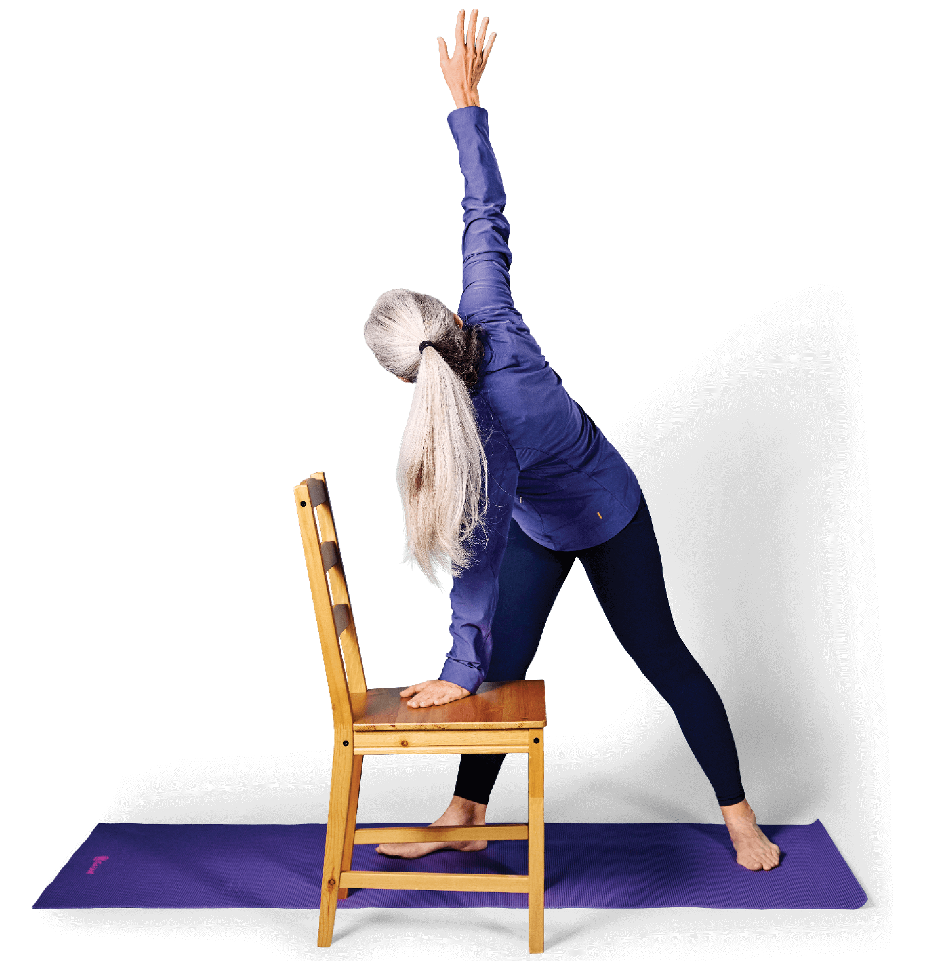 Photo of a woman in Twisted Triangle yoga pose, with one hand resting on the seat of a chair