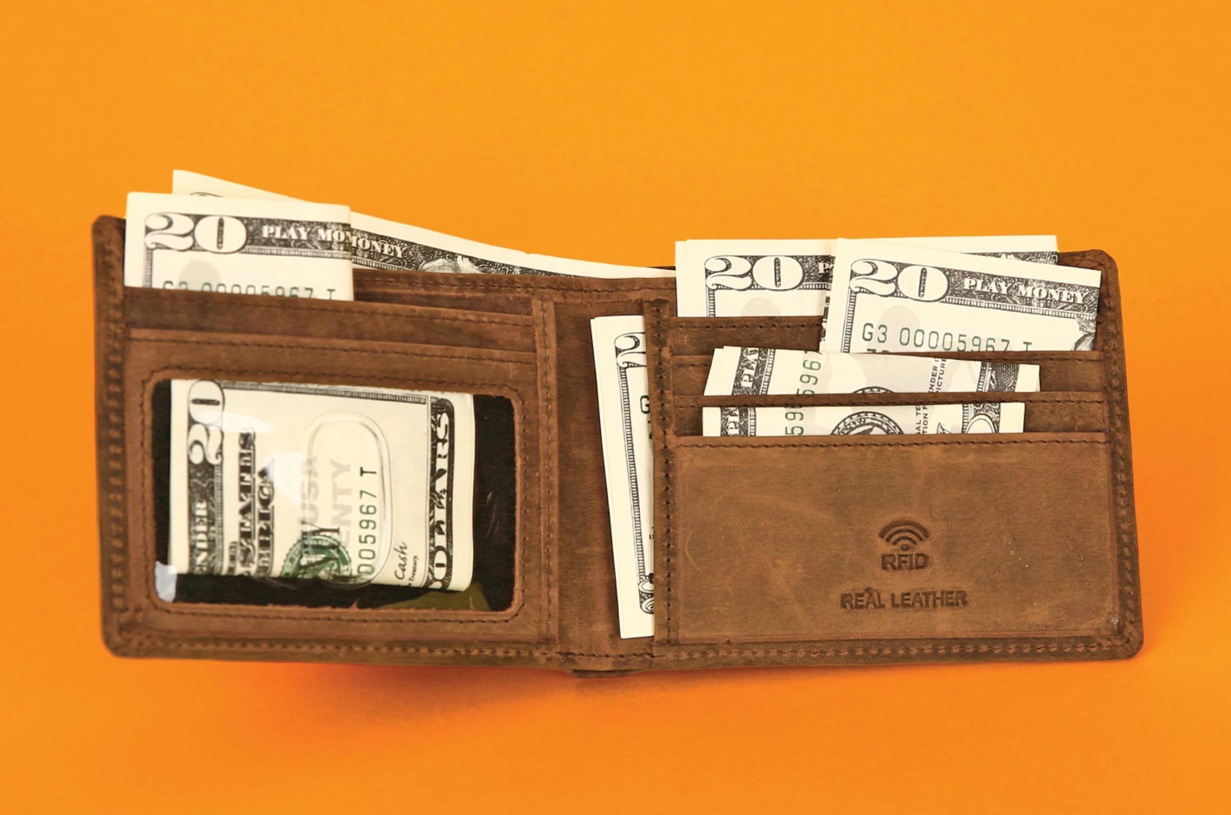 A leather wallet with twenty dollar bills stuffed in multiple compartments.
