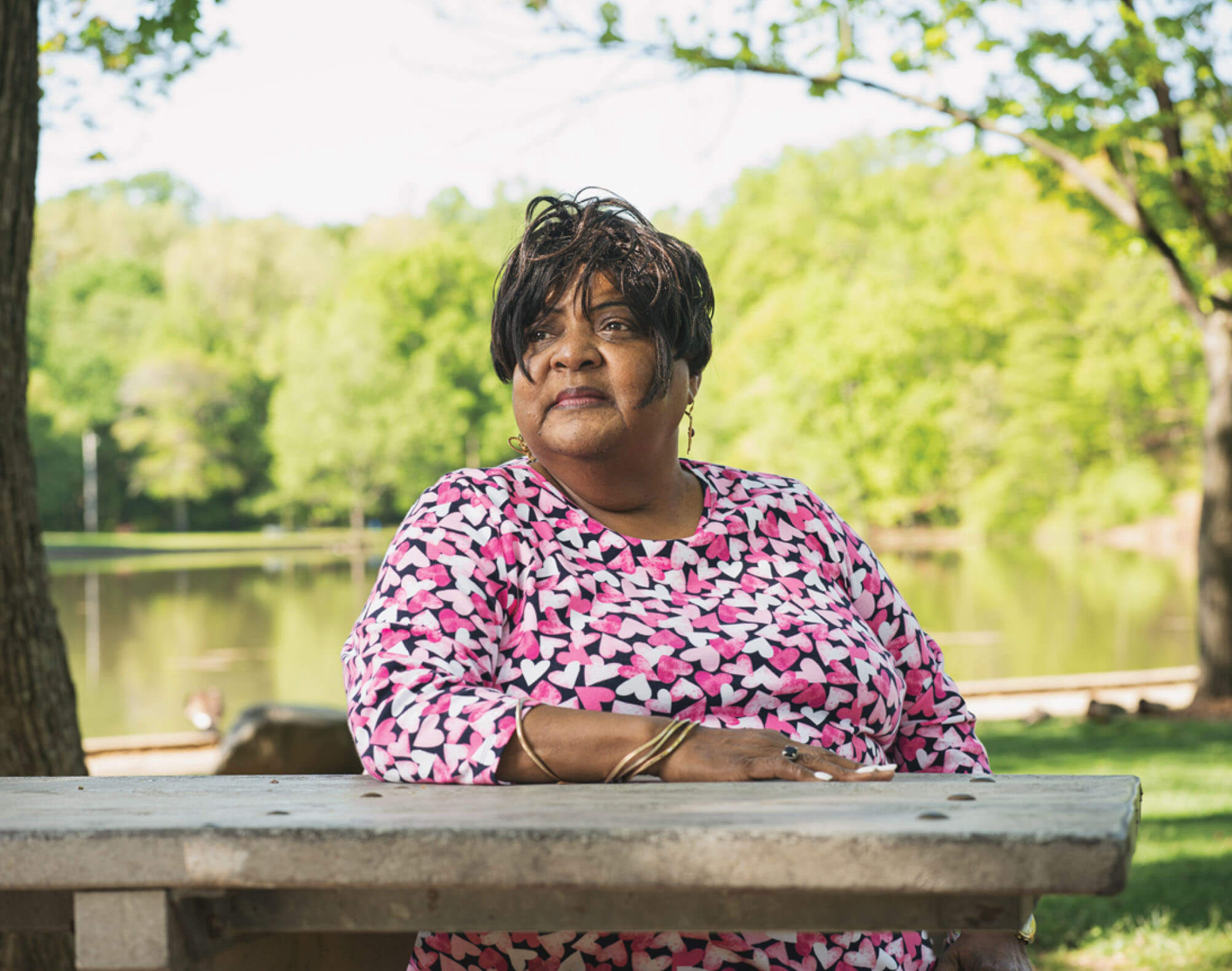 An middle aged African American woman, Dale Marshall, sitting at a picnic table in front of a lake.