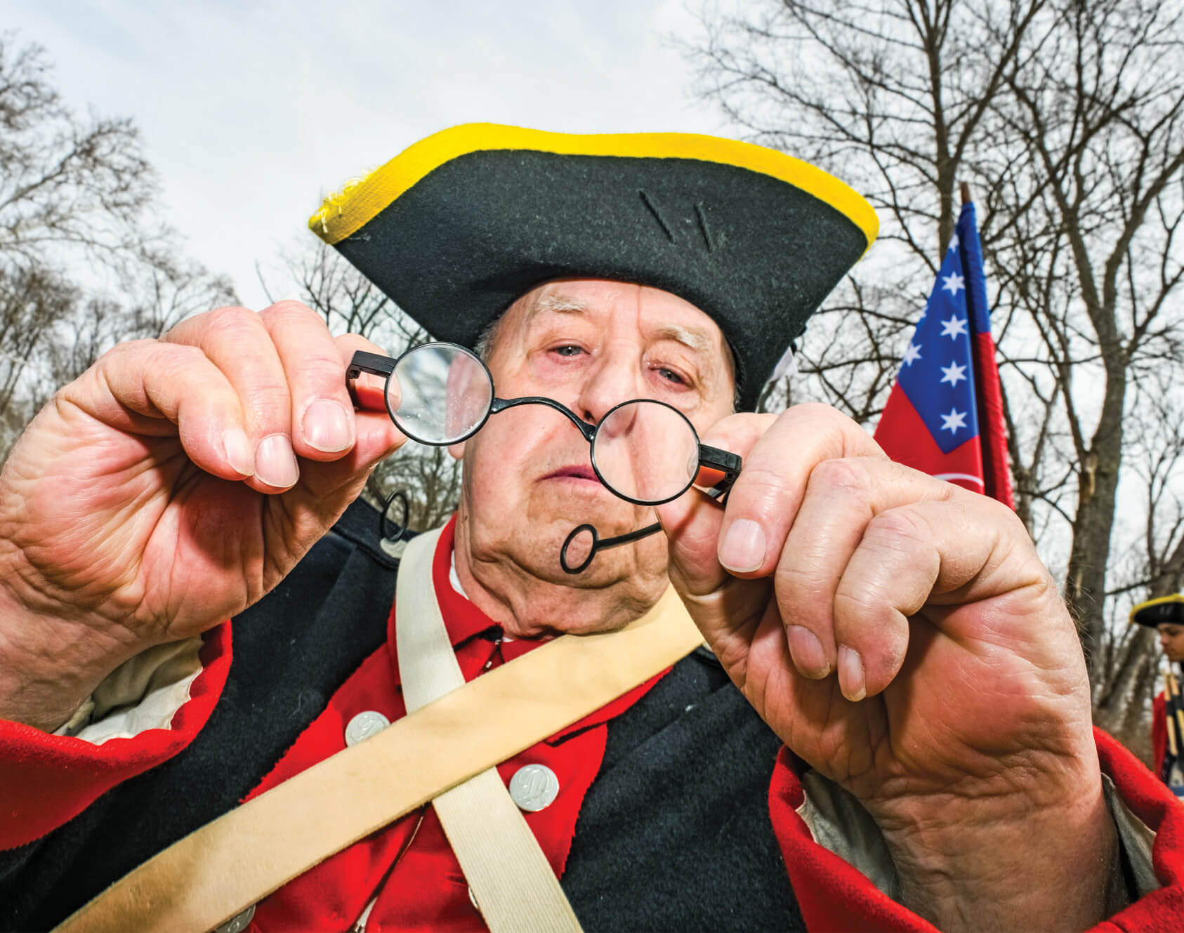 Photograph of an reenactor holding out his glasses and looking through them.
