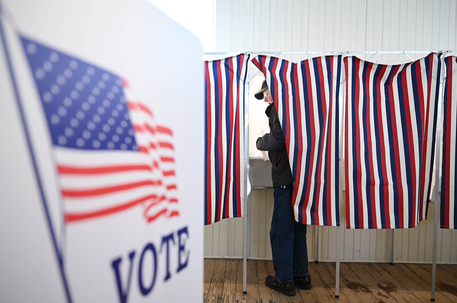 Photo of older man emergering from behind curtain of a voting booth