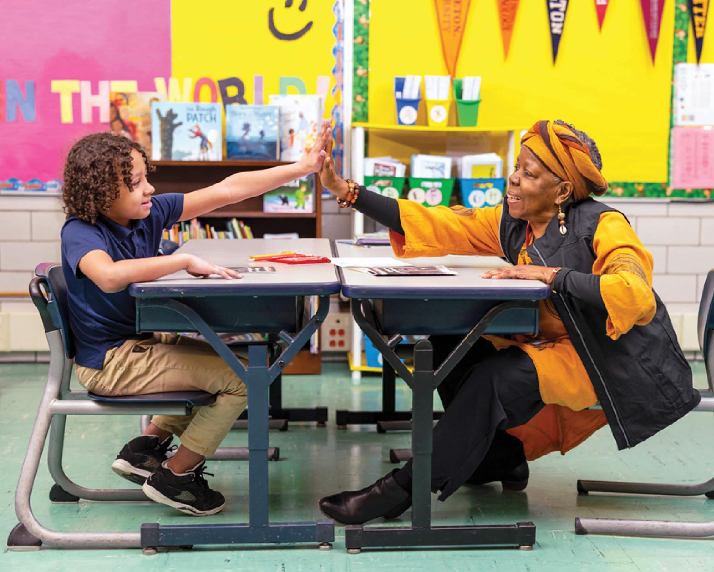 Photo of an older woman high-fiving a young student in a colorful classroom
