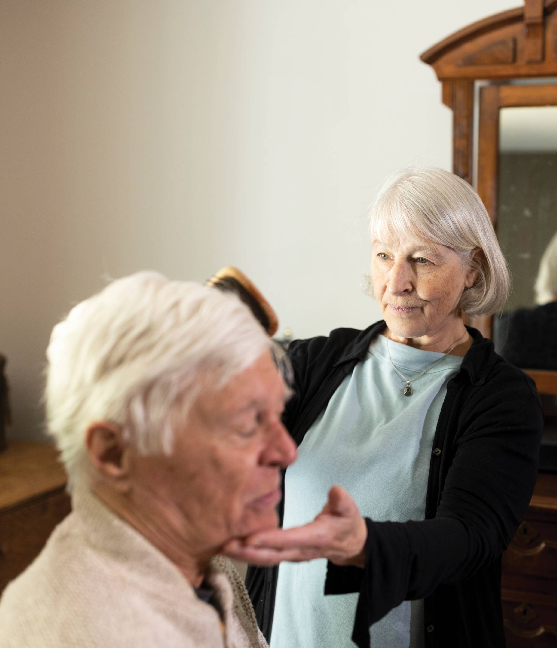 Image of Myra Spider helping her husband out in their bedroom. She is combing his hair while he sits.