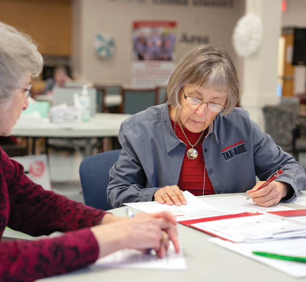 Photograph of AARP tax-aide volunteer Marylou Murry with another older women sitting at the desk going through paperwork.