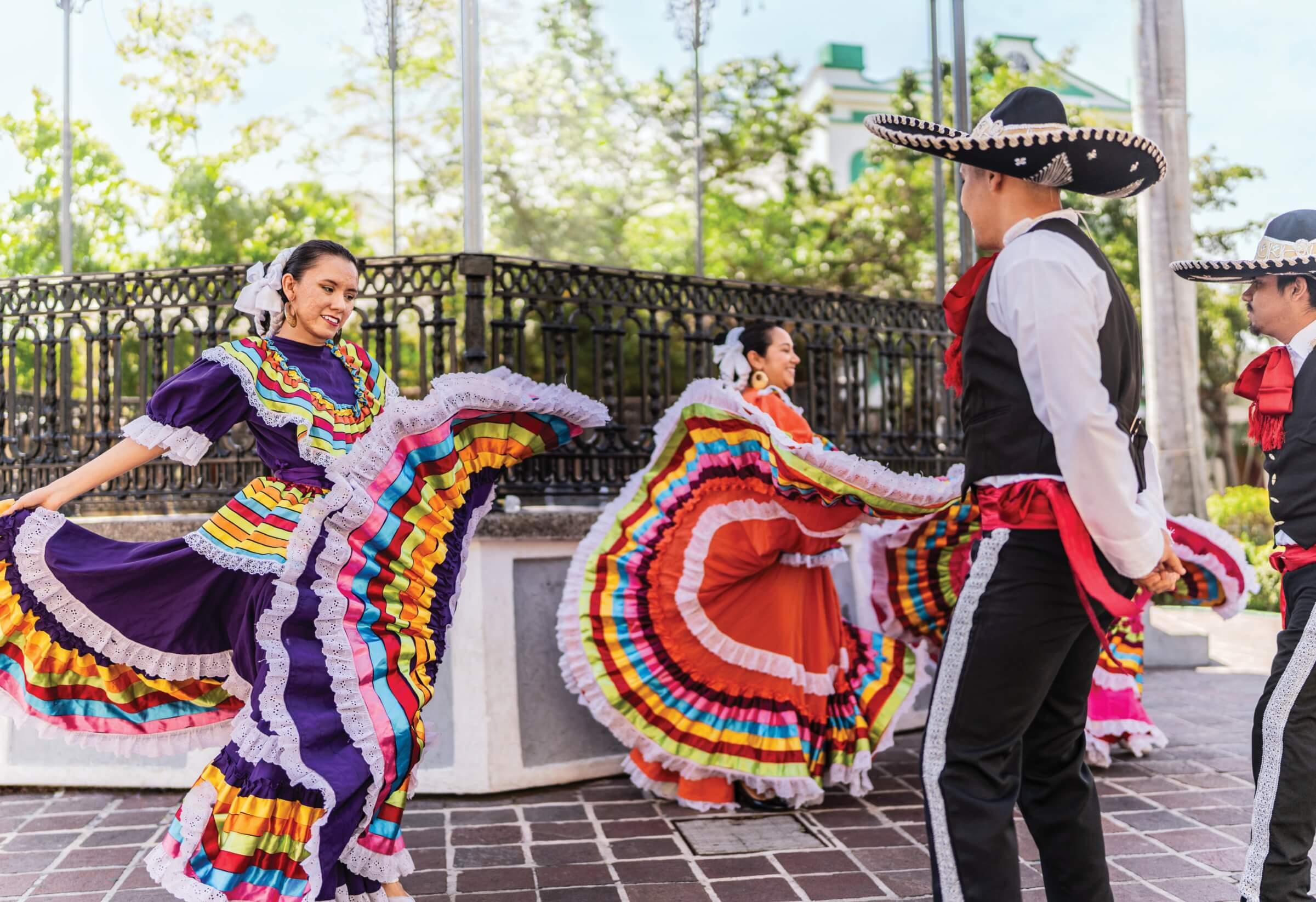 Photograph of men and women in traditional dresses and suits dancing outside
