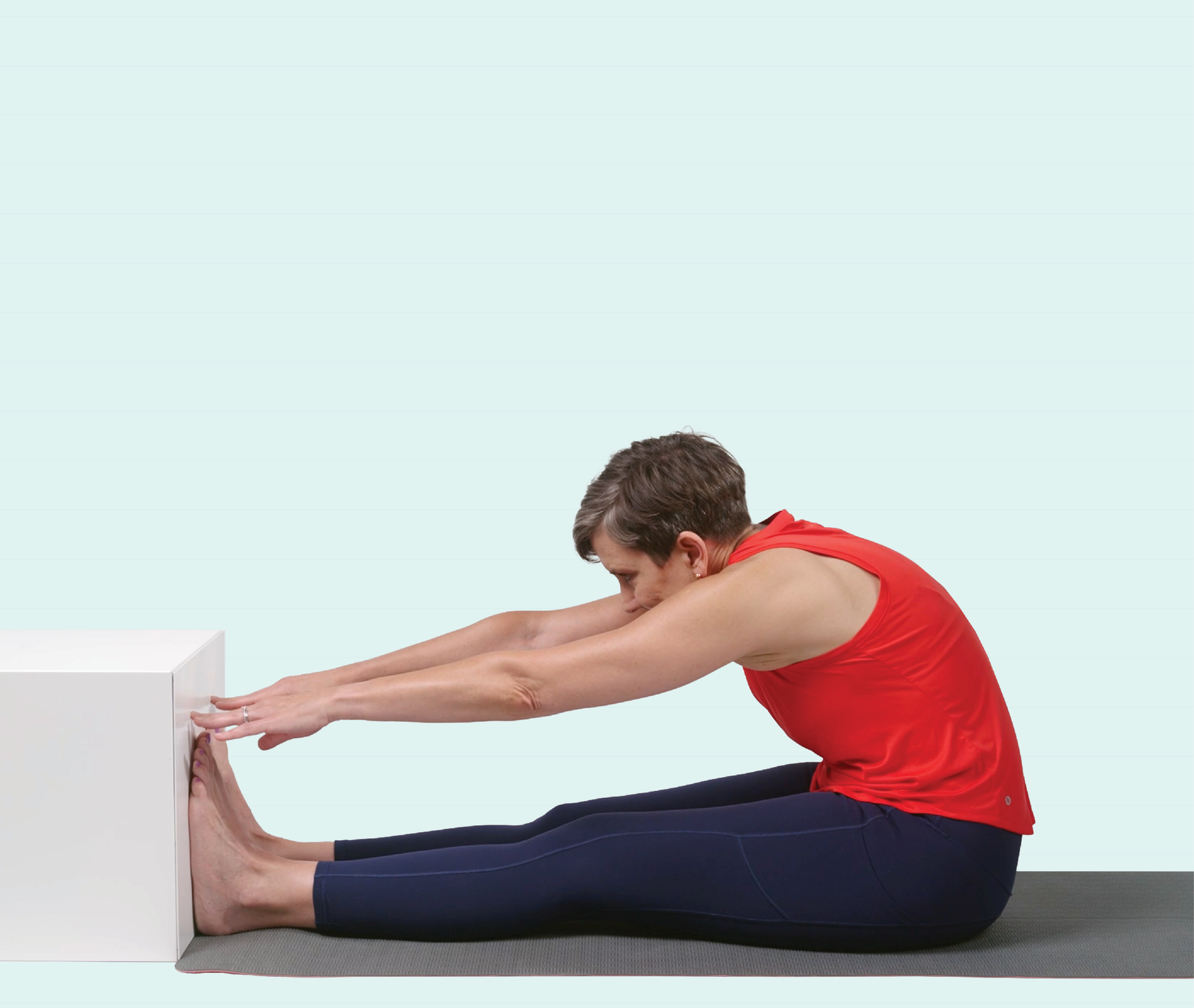 Image of a woman sitting on a yoga mat with her feet outstretched against a wall and touching her toes