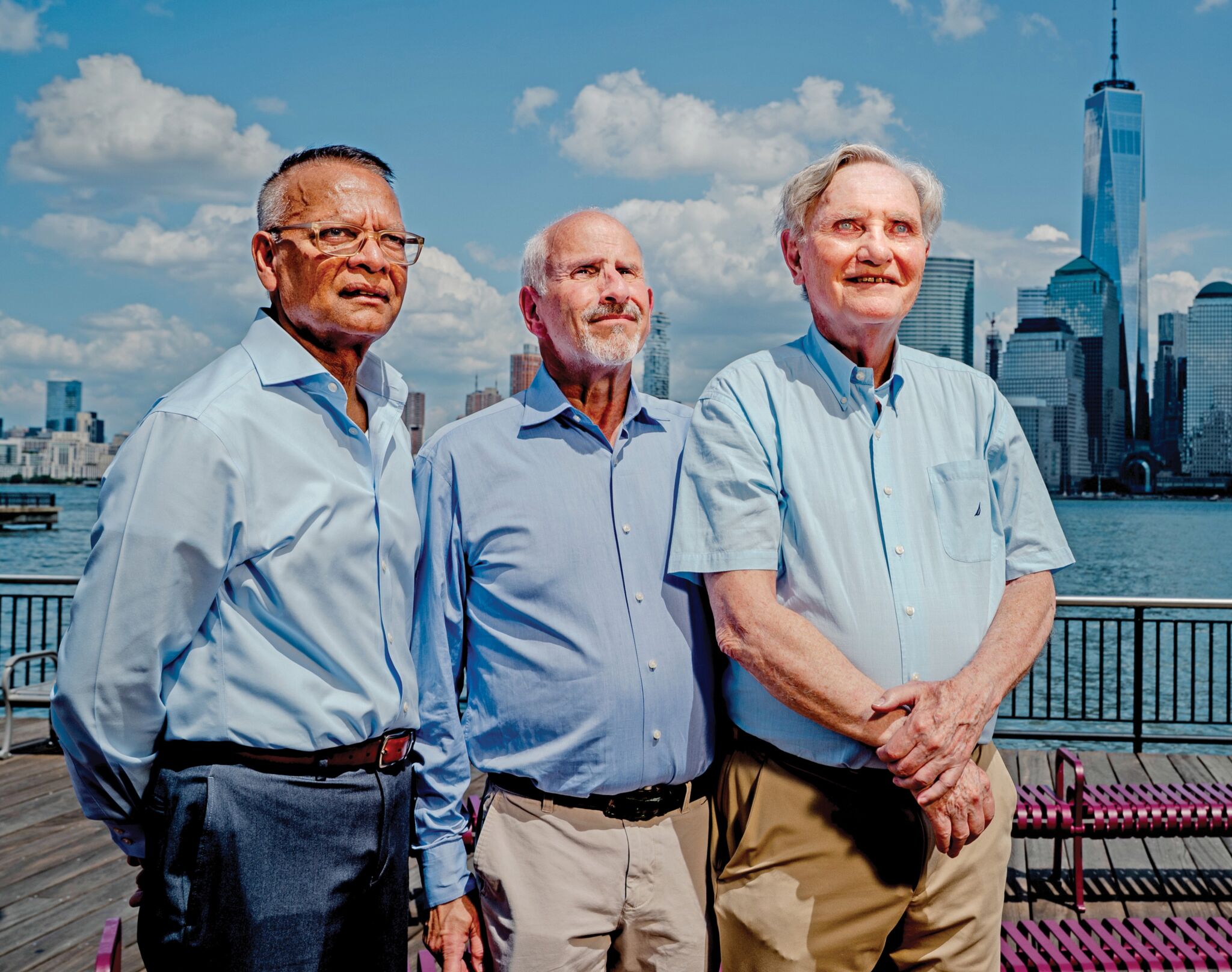 Photograph of three men smiling and standing against the skyline of New York
