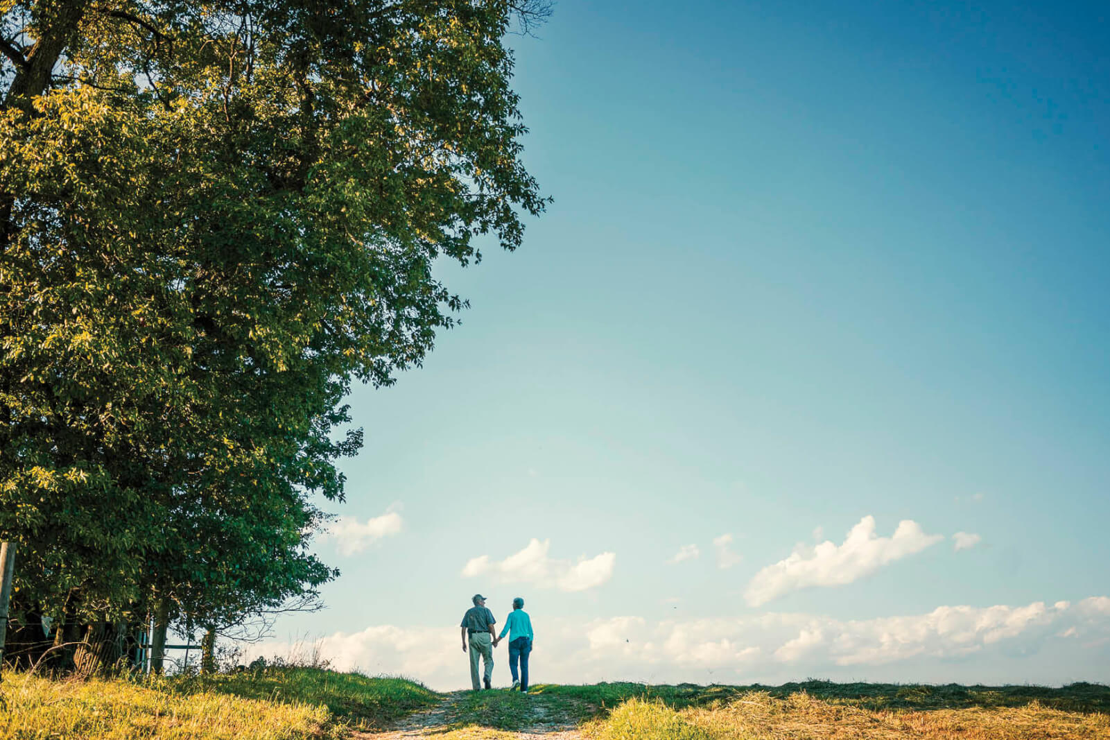 Photo of a couple walking in a large open country landscape with a blue sky in the background