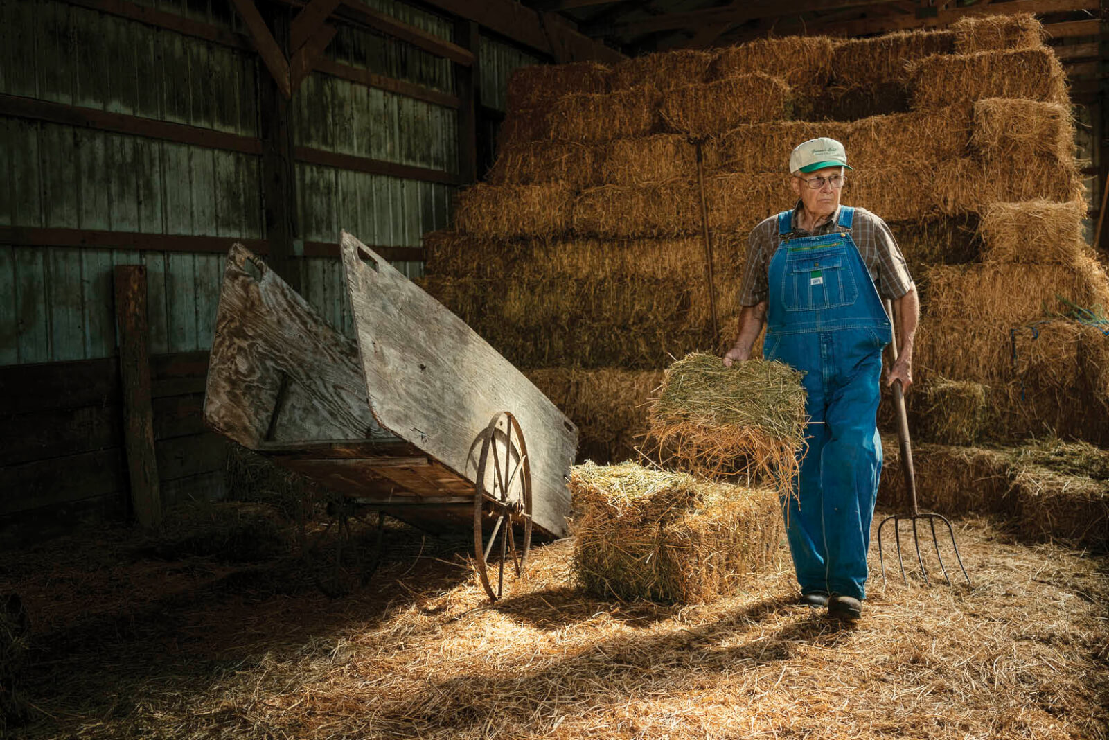 Photo of a man in a hay barn holding a bale of hay