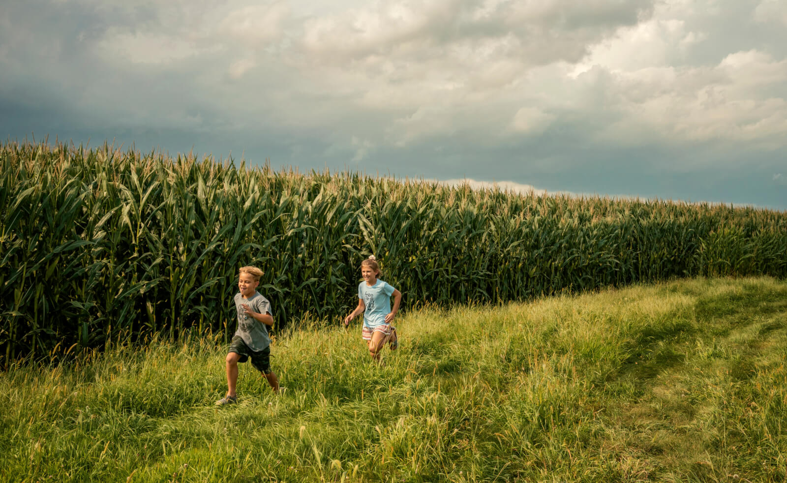 Photo of 2 kids running in a corn field