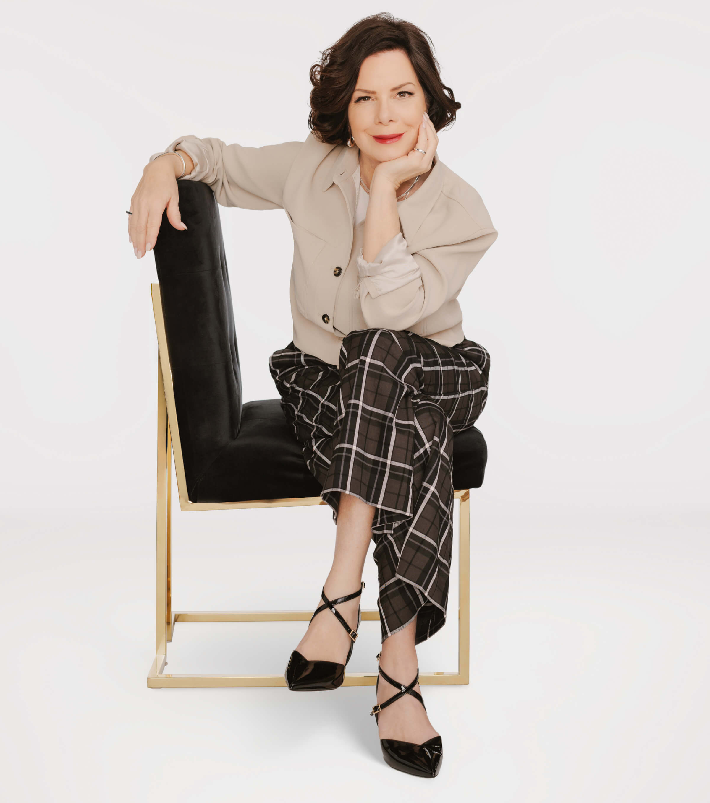 Photo of Marcia Gay Harden sitting on a chair with legs crossed and hand on her chin