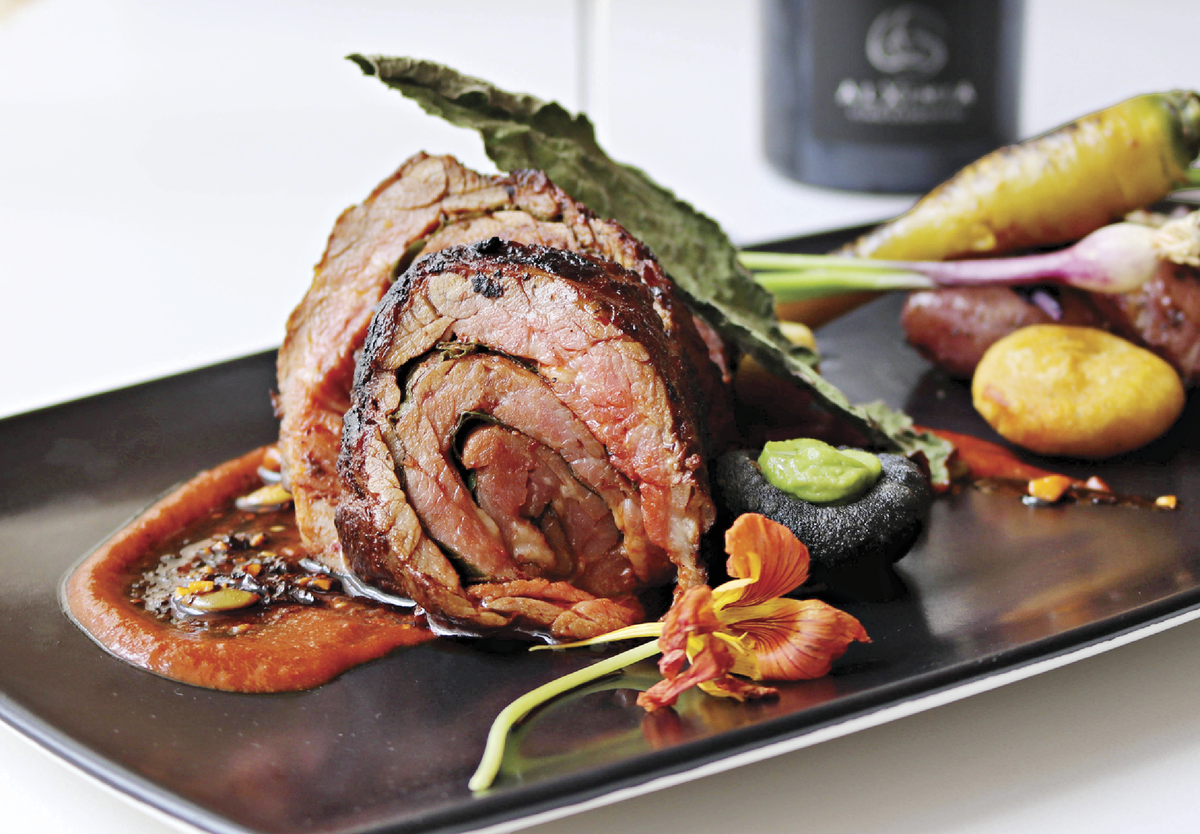 A black plate with Hugo’s barbacoa neatly plated along with greens, flowers and some veggies 