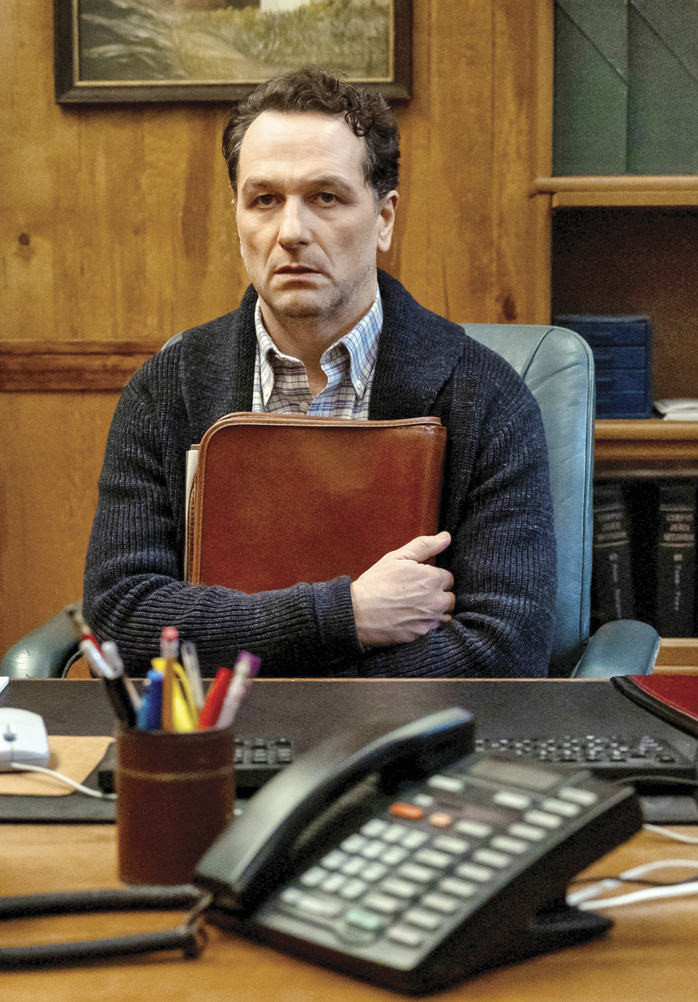 Still from Window’s Bay. Matthew Rhys is sitting at a wooden desk, clutching a leather folder and looking distantly into space