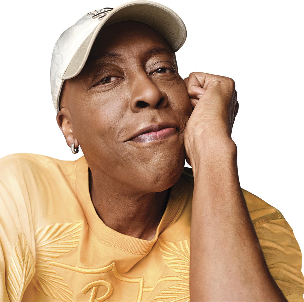 Photograph of Arsenio Hall looking into the camera and smiling. He is wearing an orange t-shirt a beige LA cap.