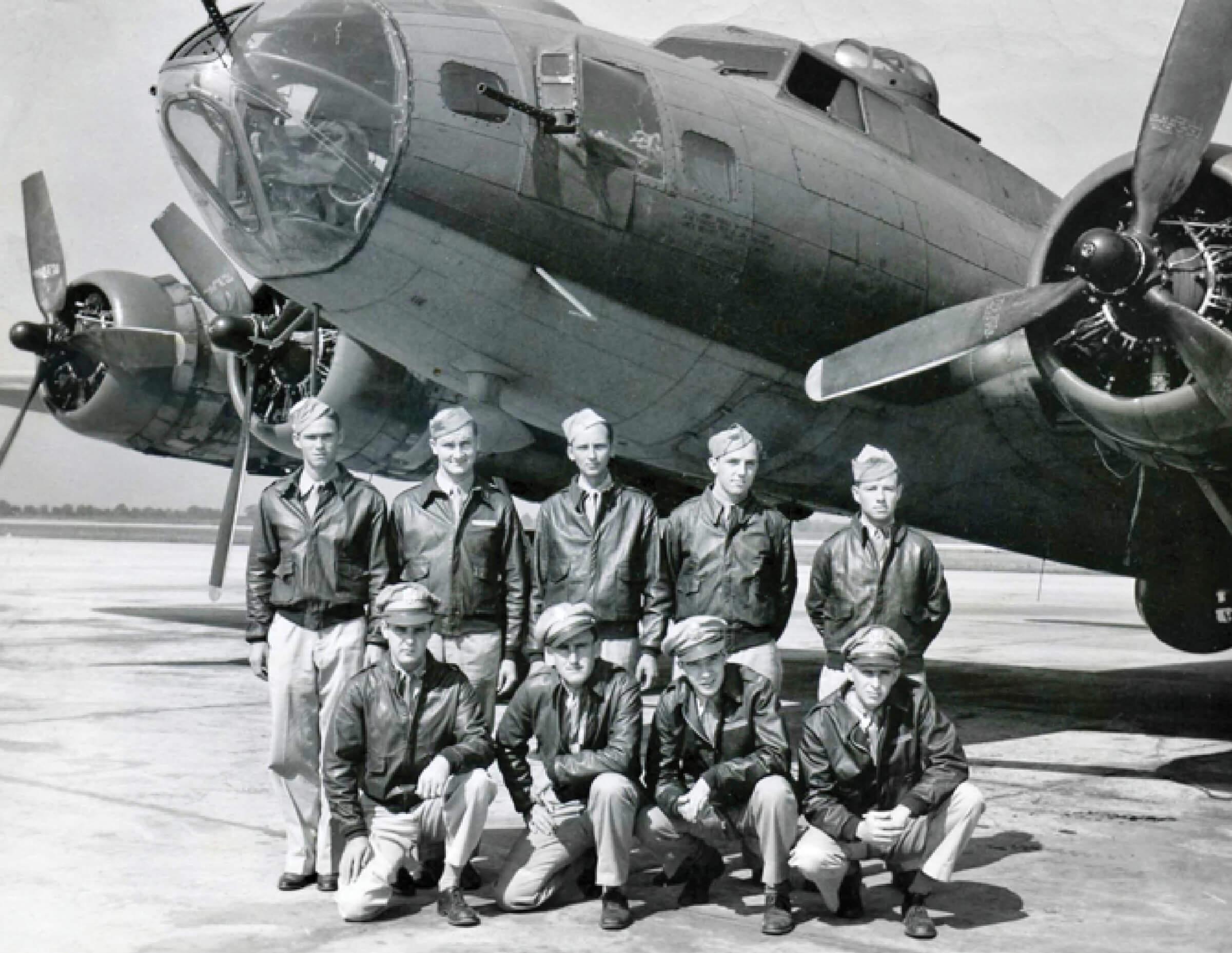 An old black and white photograph of a squad of 9 soldiers sitting in front of a B-17 during training 