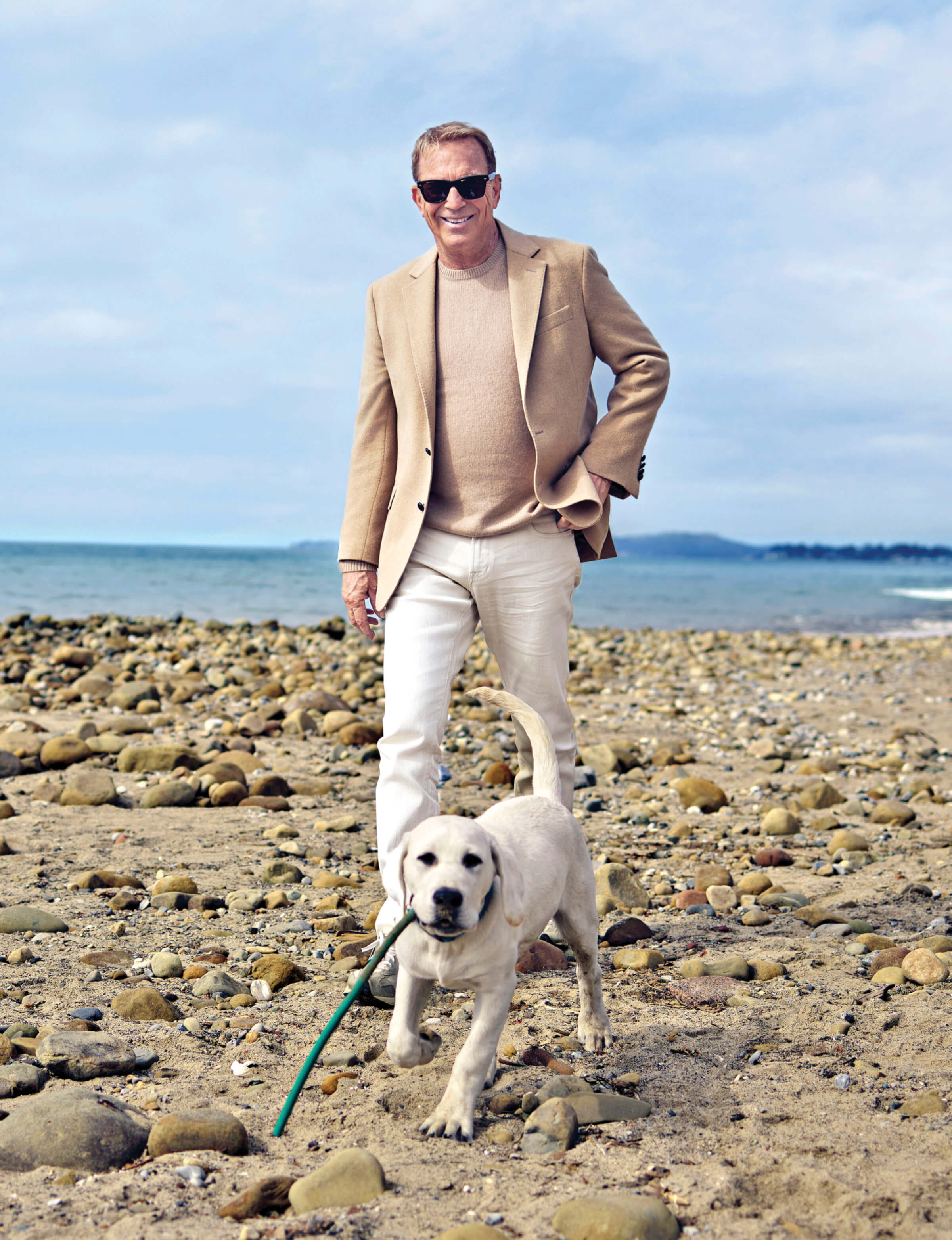 Photo of Kevin Costner on the beach with a white labrador puppy