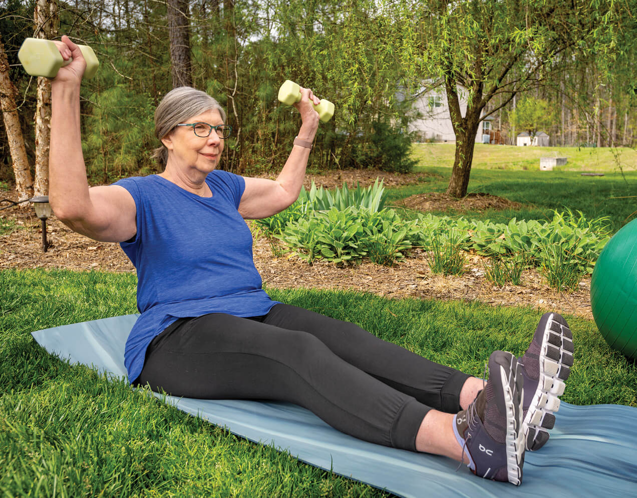 Photo of Angela seated on a yoga mat and lifting dumbbells