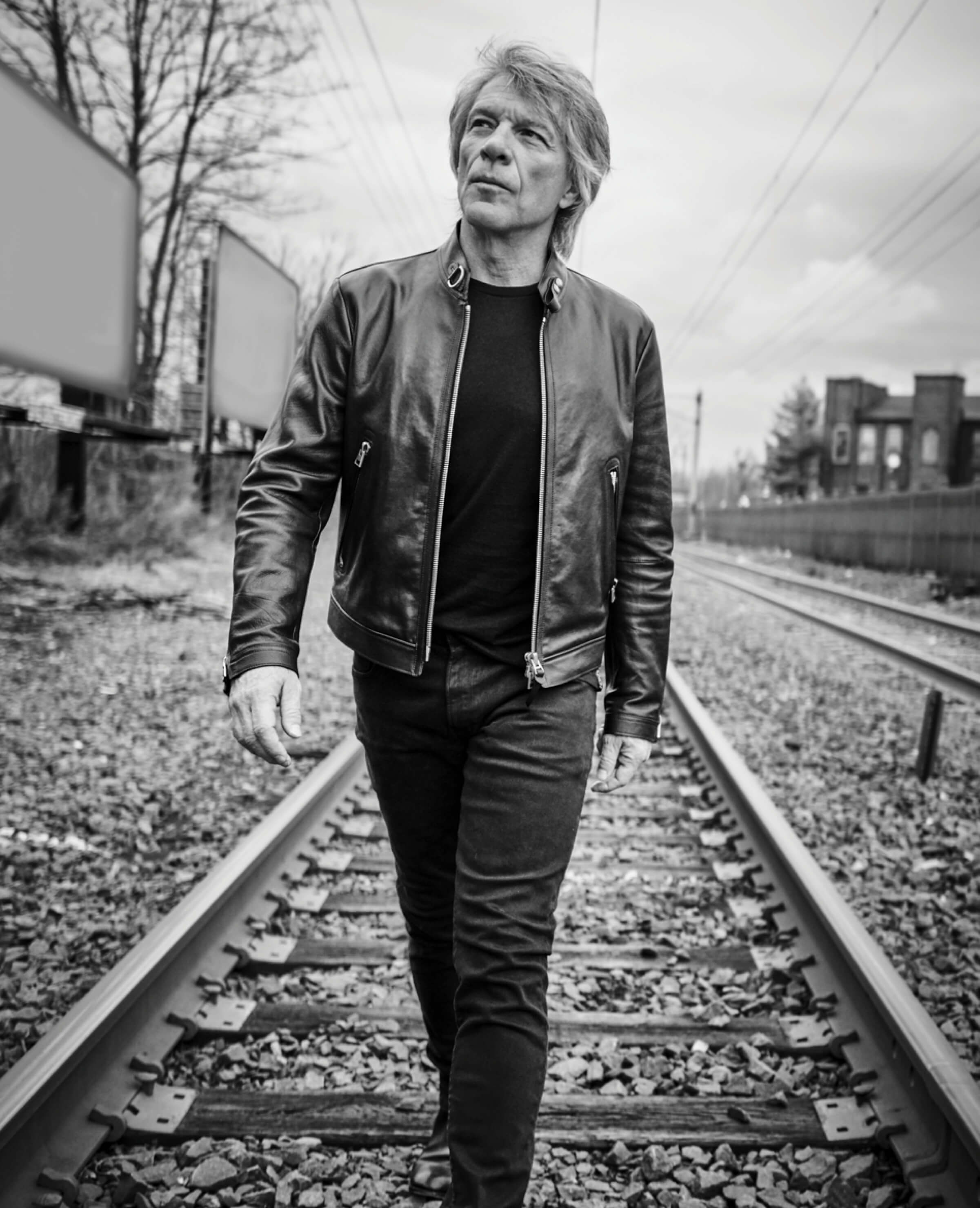 Black and white photo of Jon Bon Jovi walking near train tracks