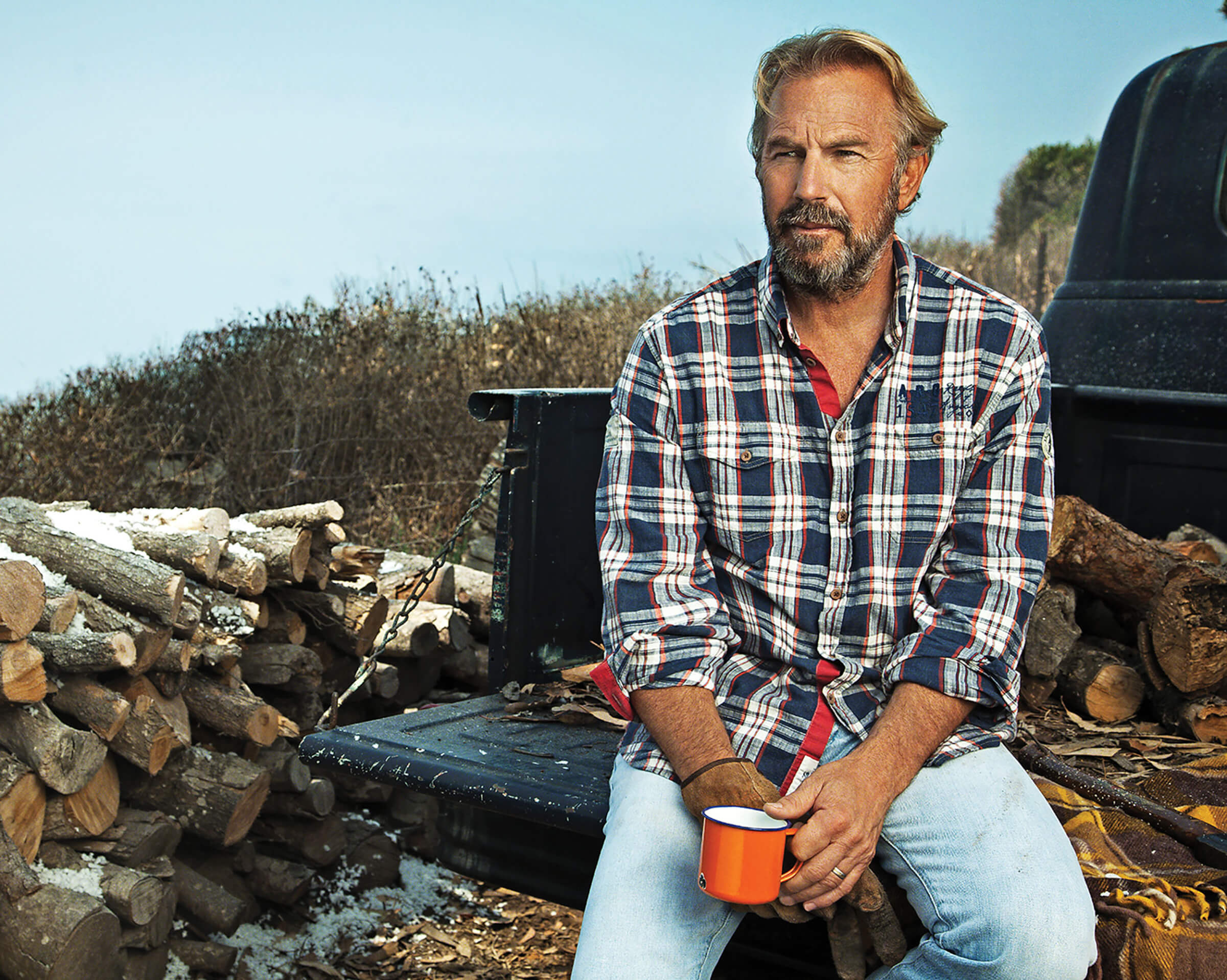 Photo portrait of Kevin Costner sitting on an open truck bed with firewood