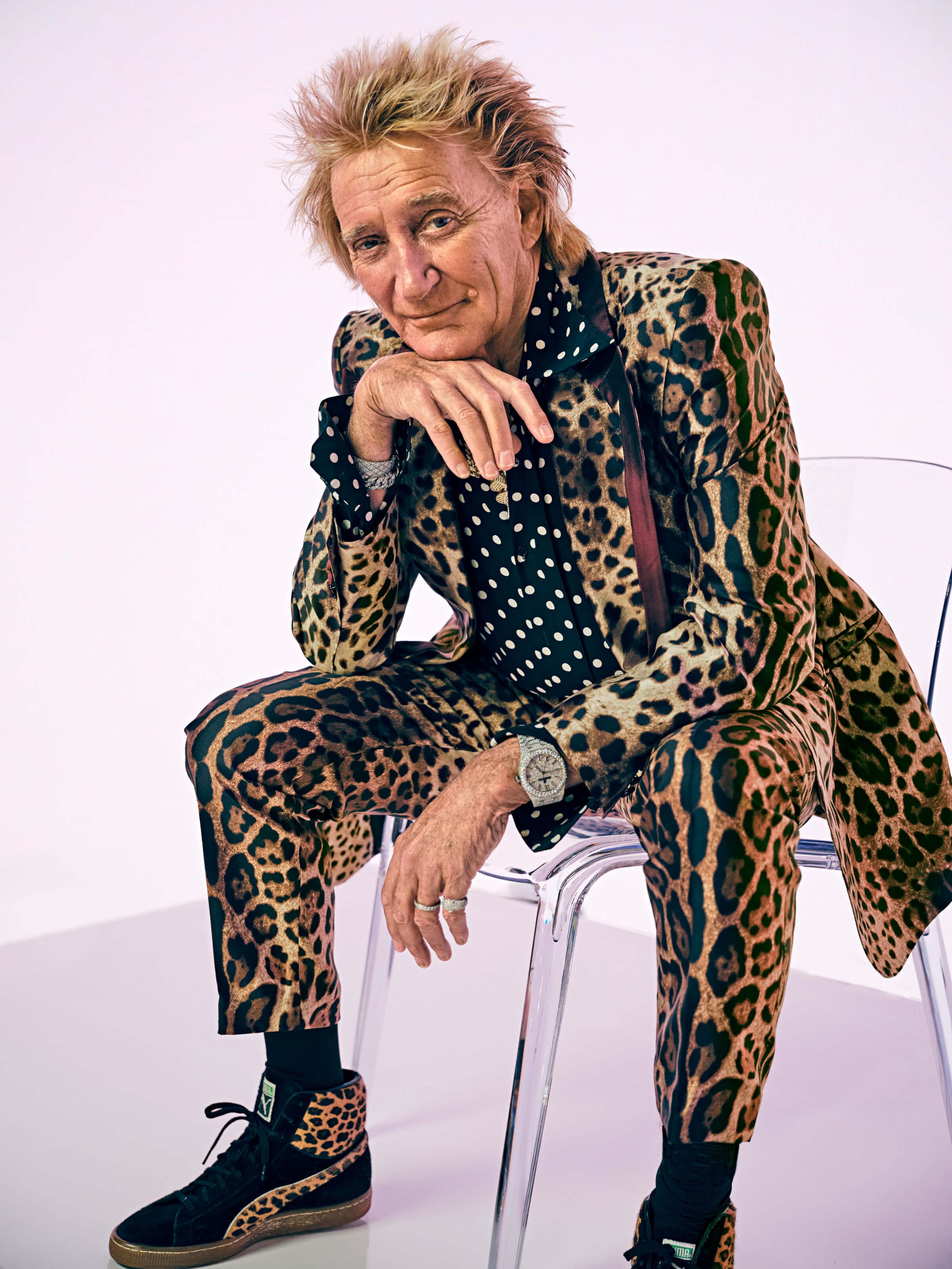 Photo portrait of Rod Stewart. He is wearing a leopard print suit and sitting in a chair
