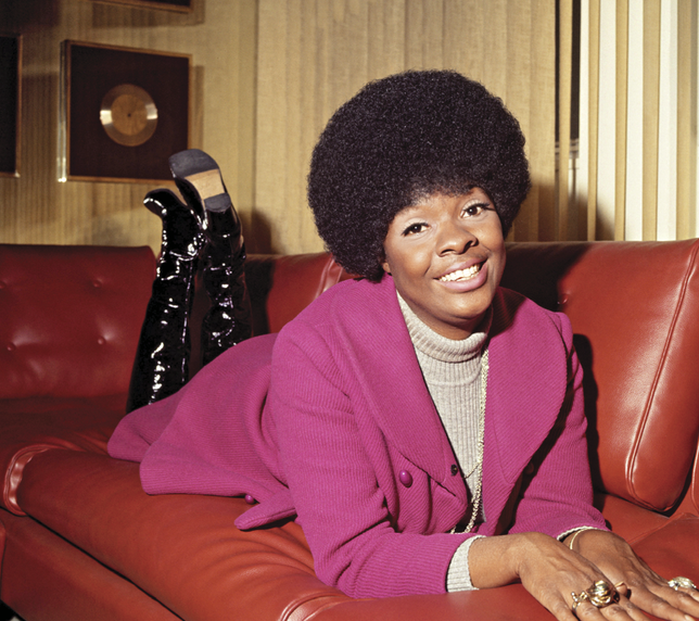 Older photograph of her laying on a couch in a pink blazer 