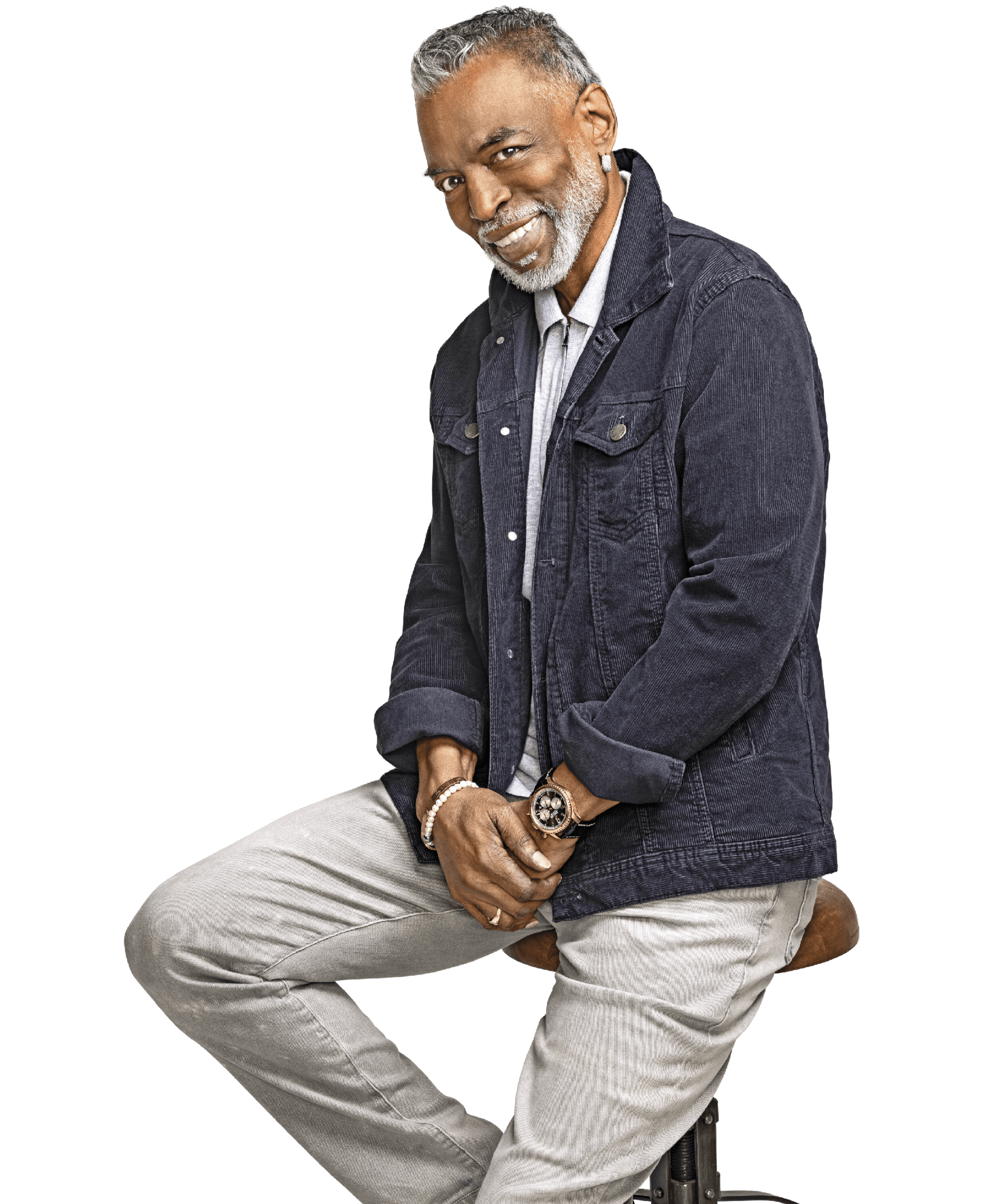 Portrait of Levar Burton sitting on a wooden bar stool. He is wearing a grey/blue denim jacket and grey pants