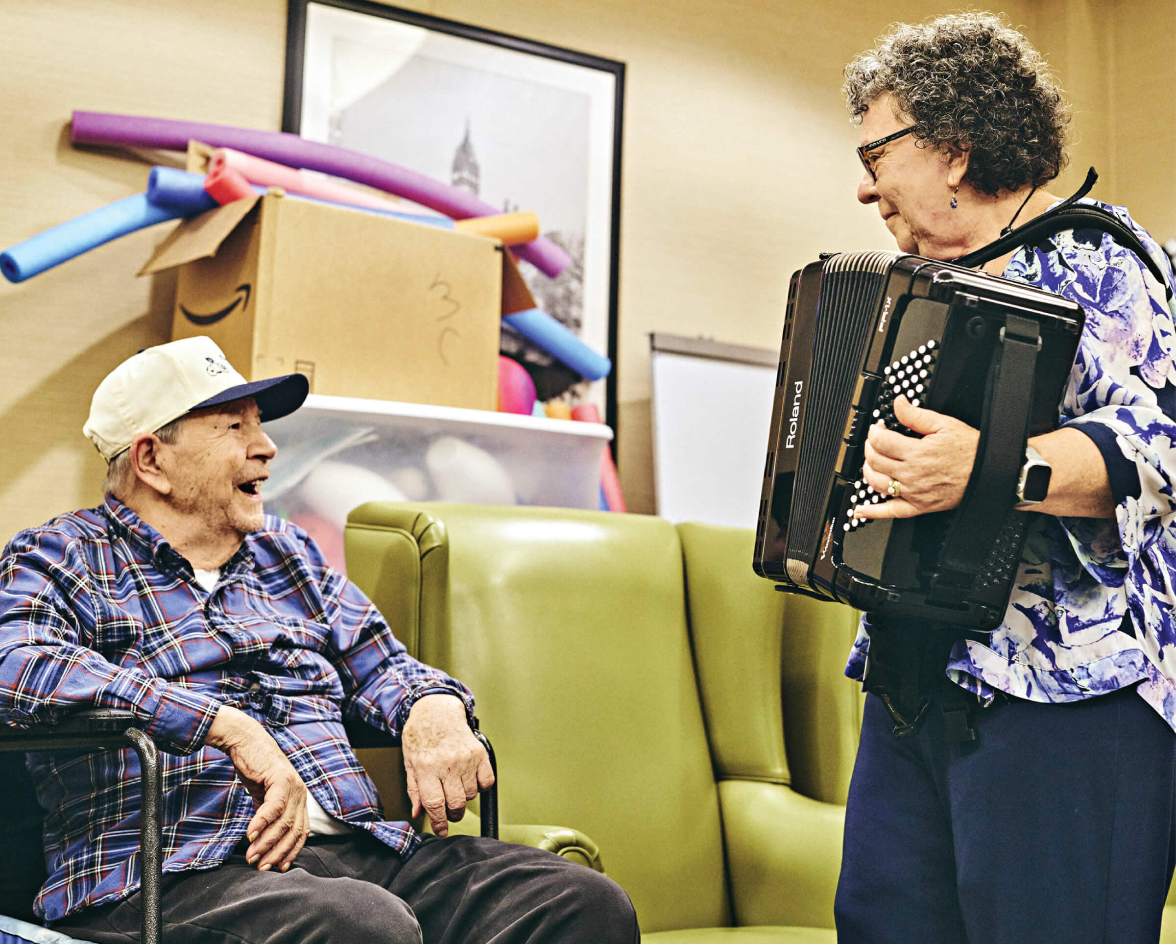 Photo of Concetta Tomaino playing her accordion for an elderly man at a senior living facility