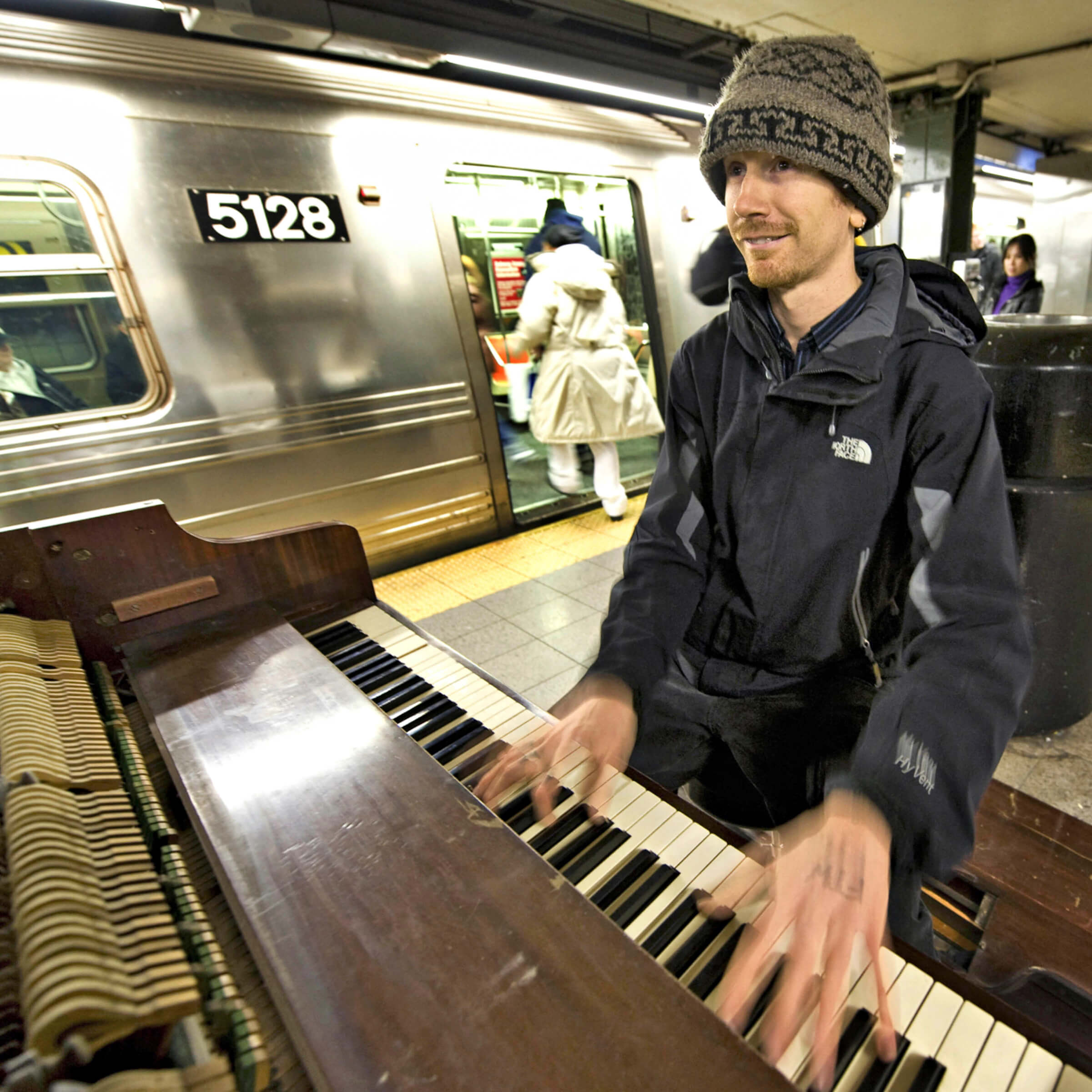 Photo of Colin Huggins playing his piano on a New York City subway platform