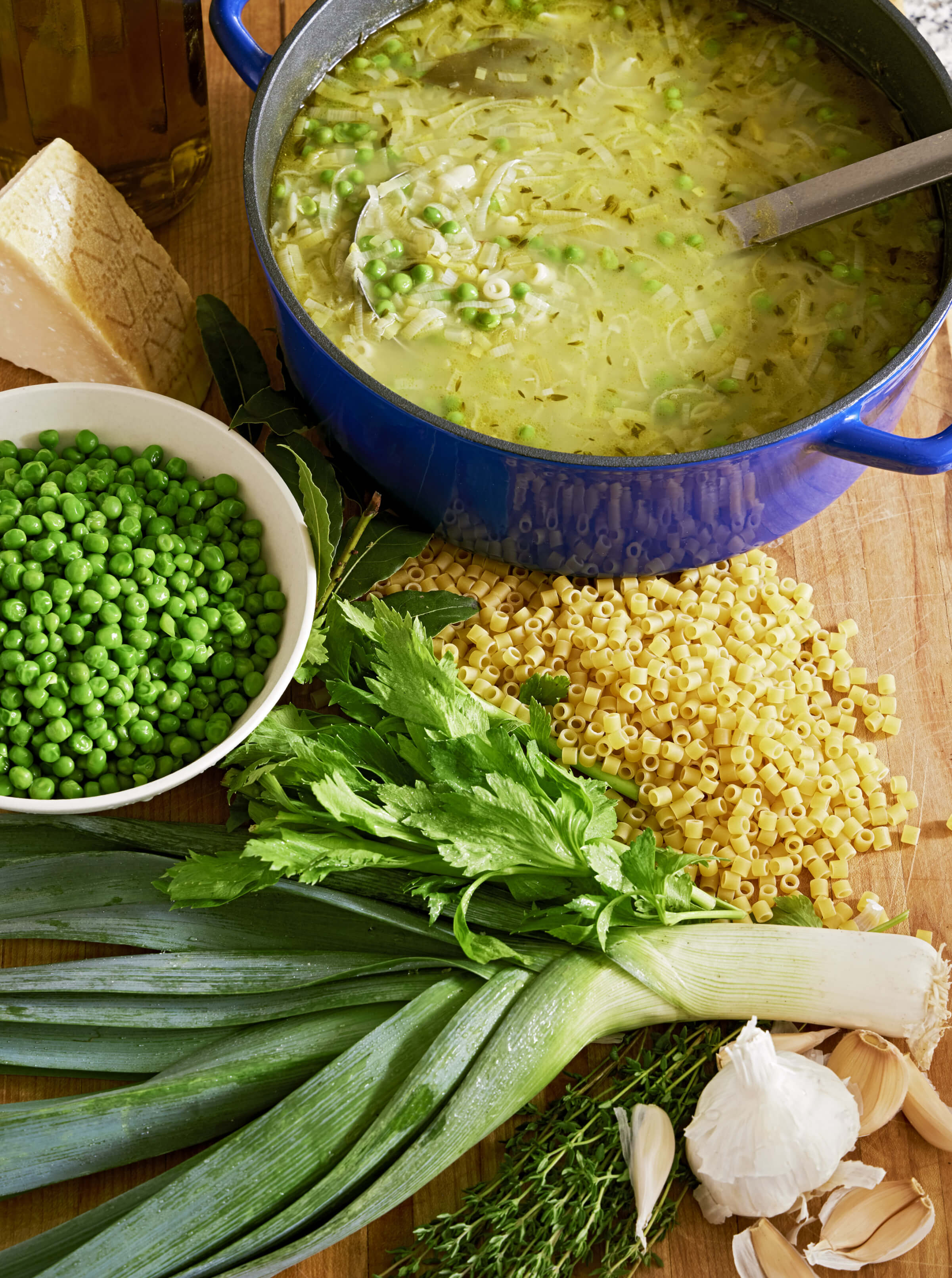 Photo of a big pot of pea soup with peas, leeks, pasta, cheese and fresh herbs on the table beside it