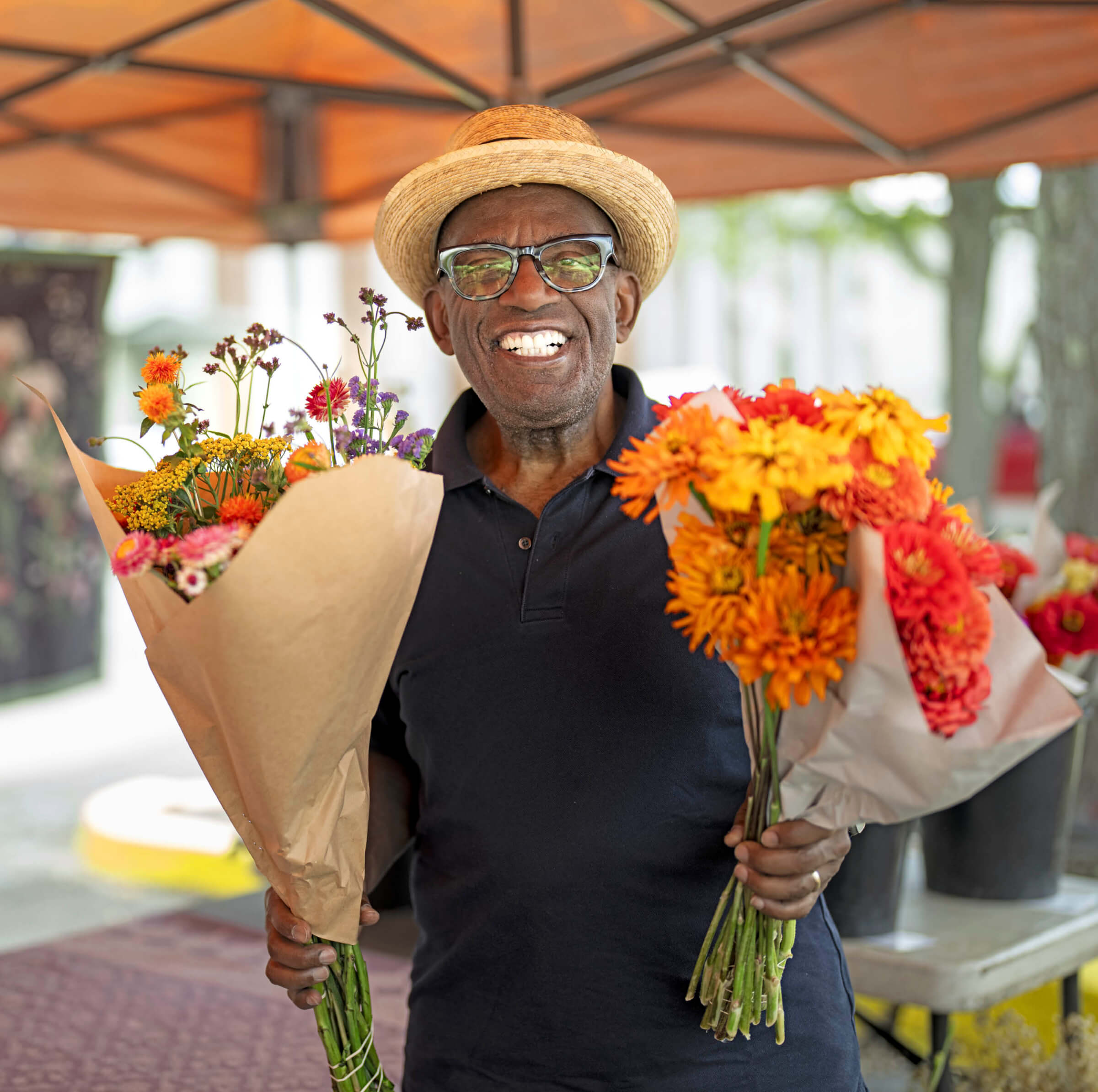 Photo of Al Roker holding two bouquets of cut flowers at a farmers market