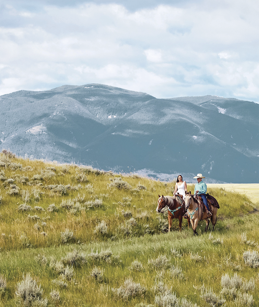 Photograph of the sprawling mountains with a man and a woman riding horses in Wyoming 