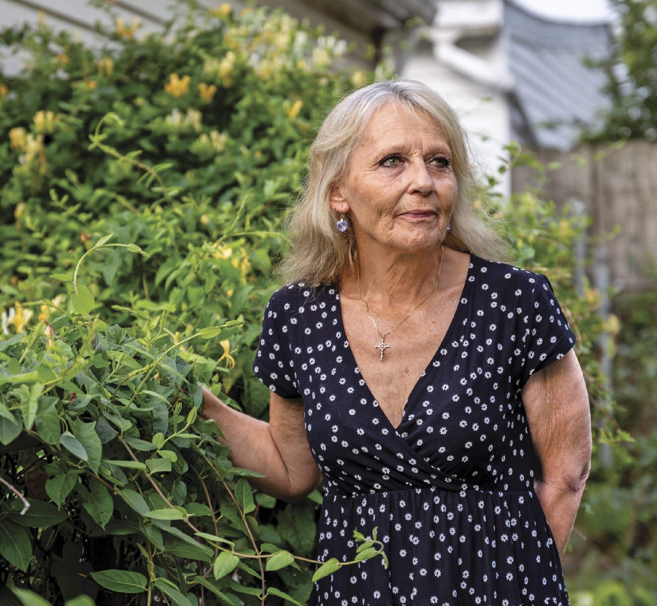 Image of Tonia Yates standing in a yard around plant with yellow flowers, looking away from the camera.