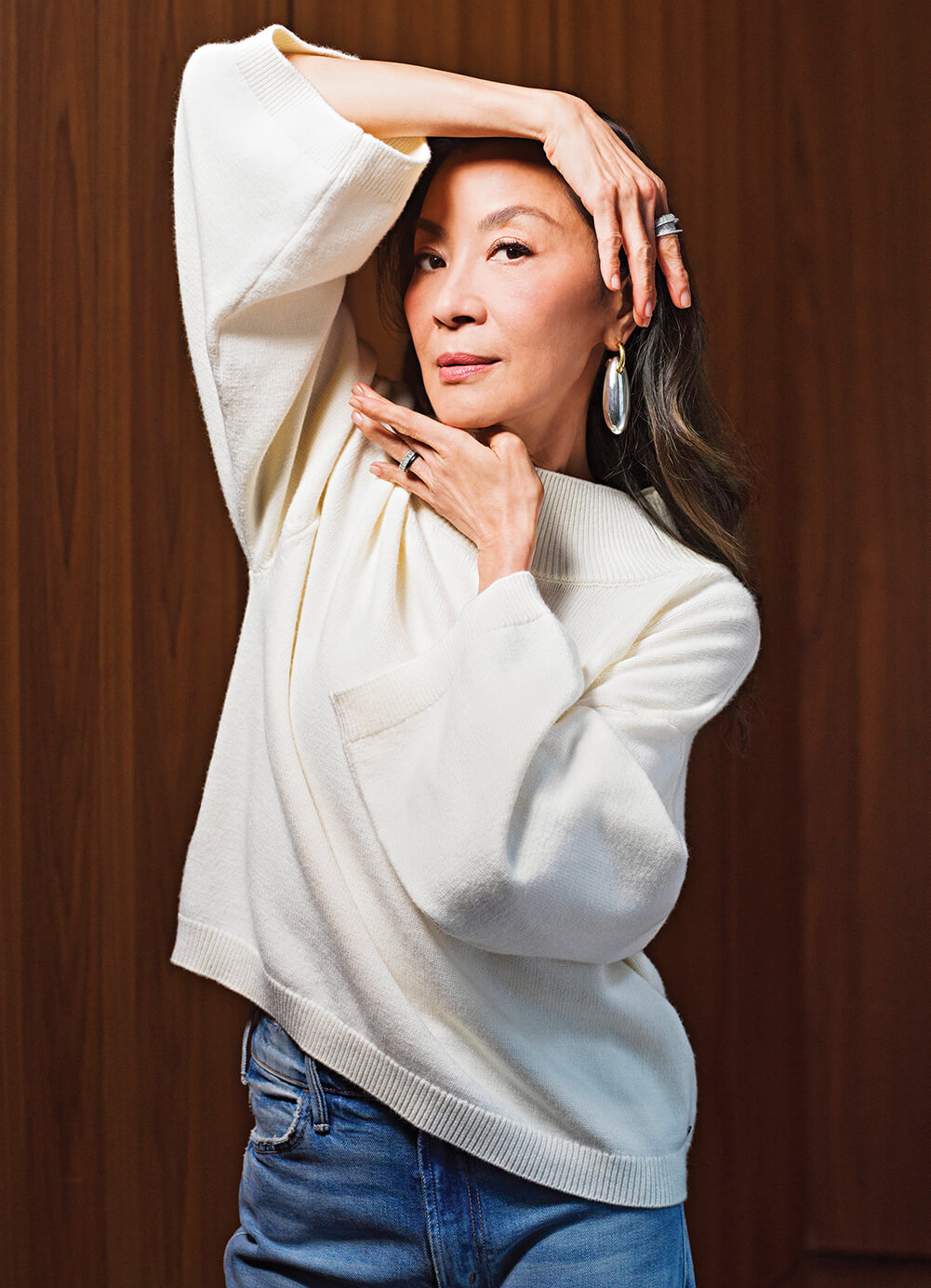Photo of Michelle Yeoh in a white sweater, using her hands to frame her face