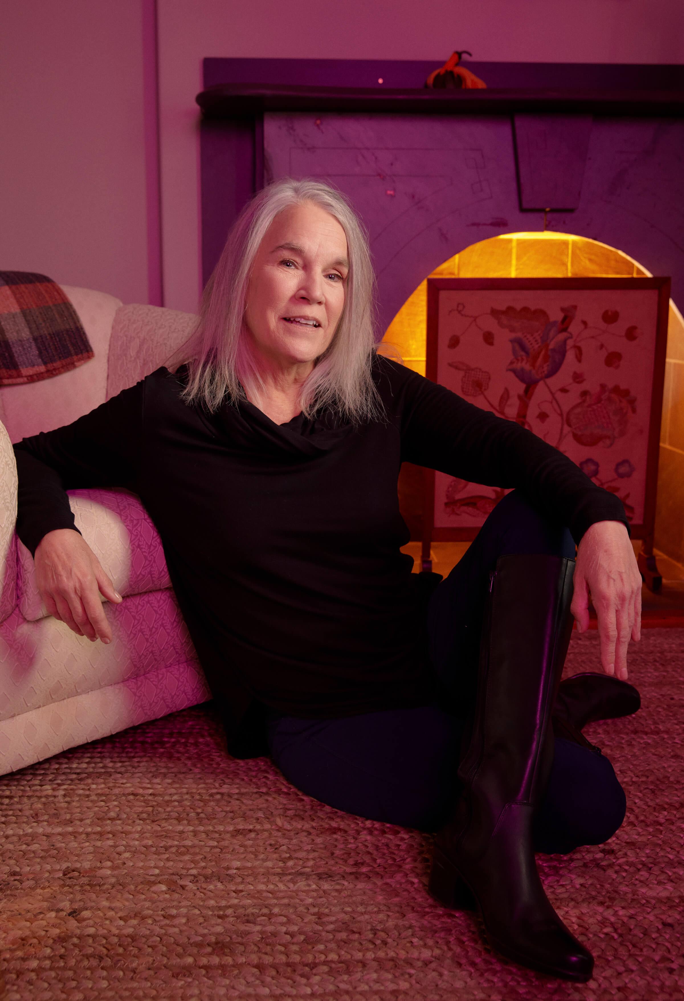 Image of Ellen Uzelac sitting on the ground in front of a couch.