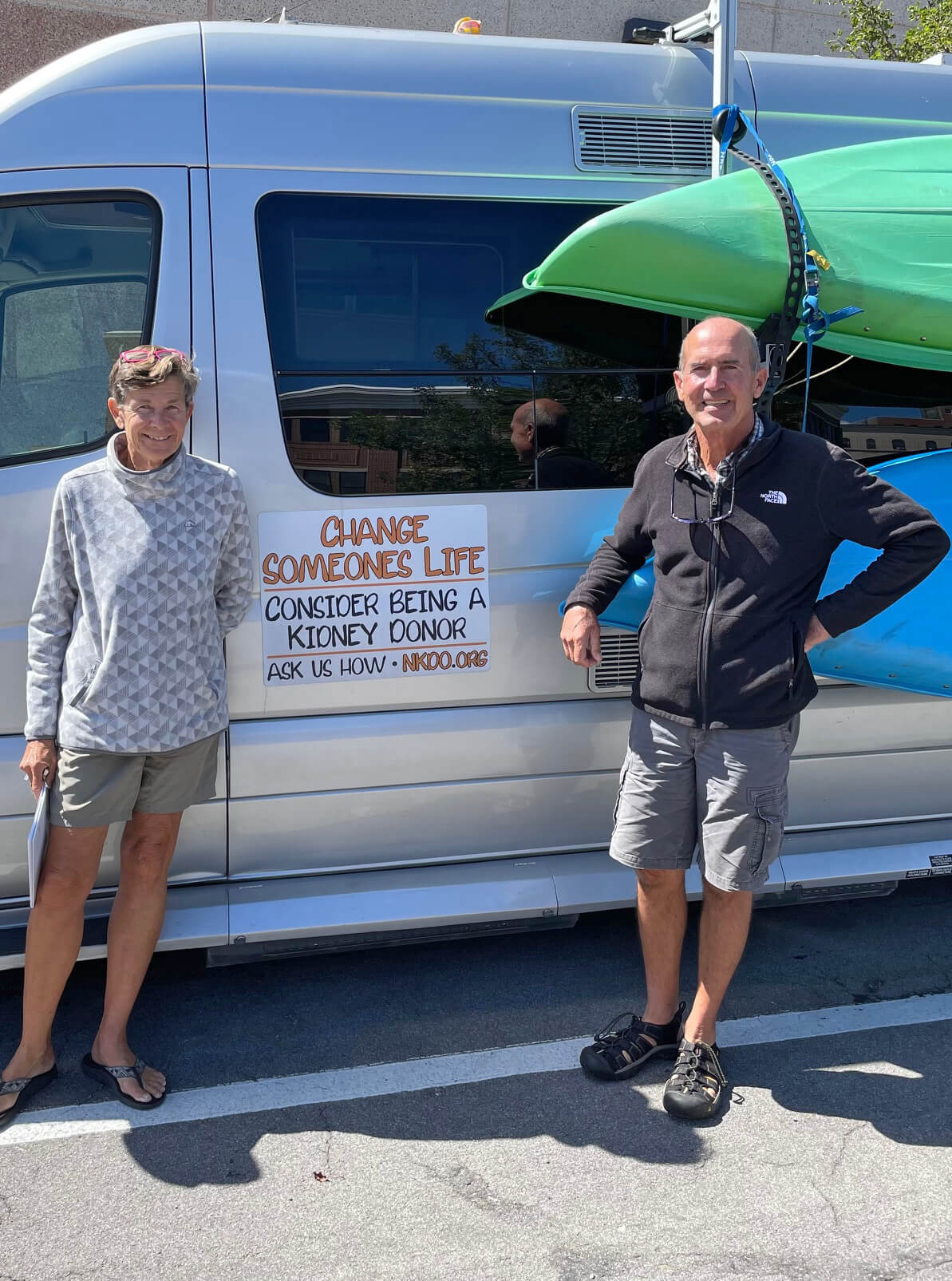 Image of Betsy and Peter Snow in front of a truck with a sign that says “Change someone’s life, consider being a kidney donor”.