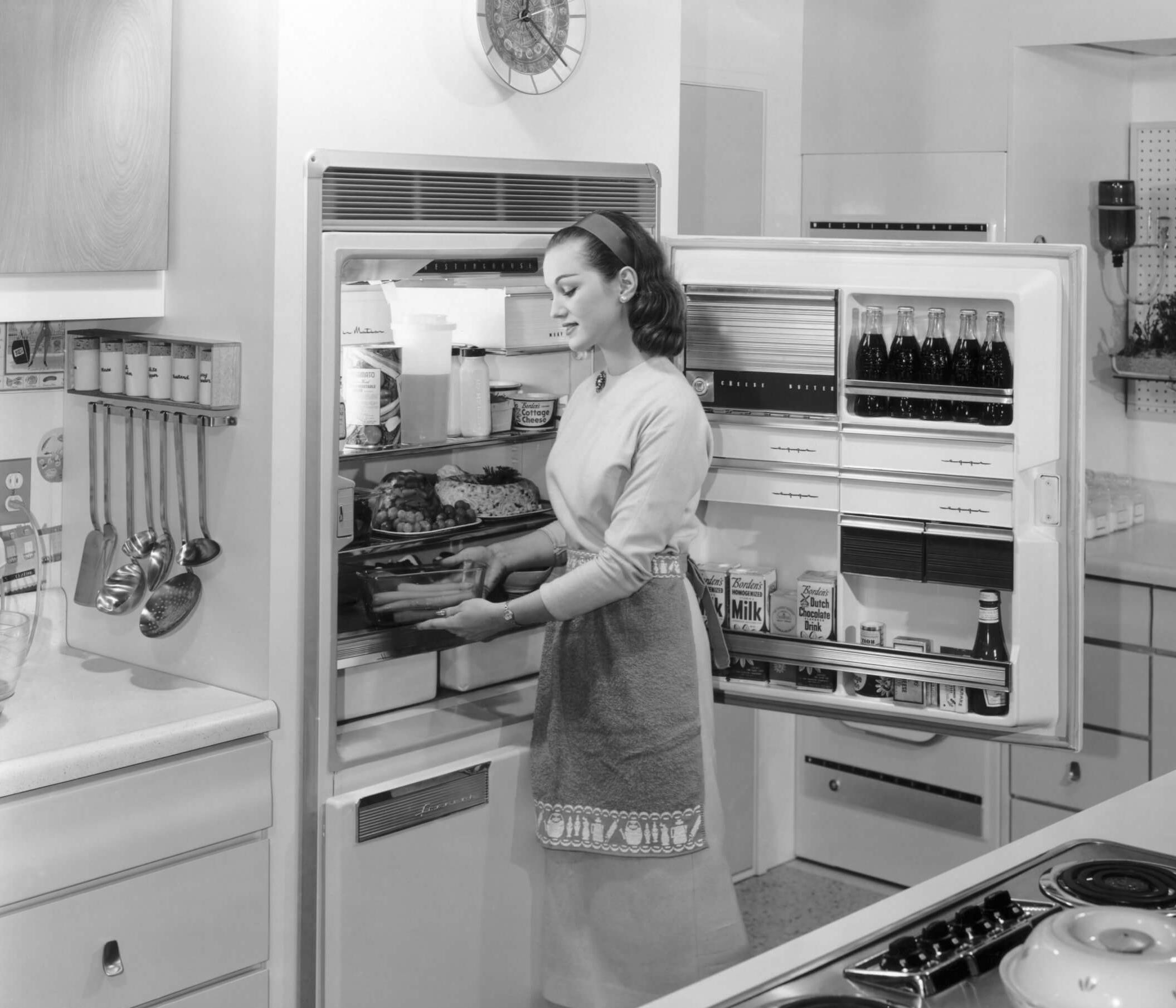 Vintage black and white photo of a woman reaching for items in a refrigerator