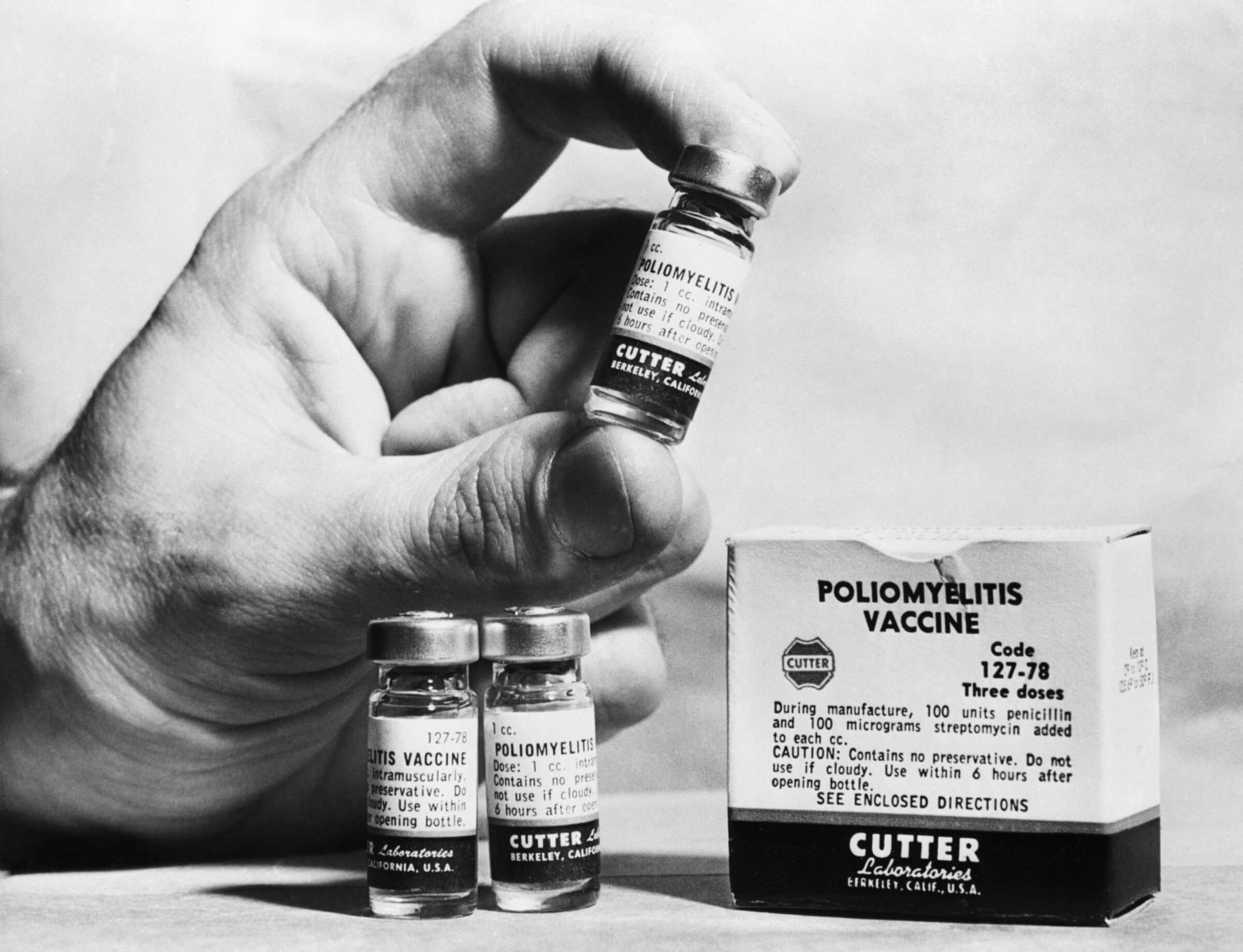 Vintage black and white photo of a hand holding a small bottle of polio vaccine