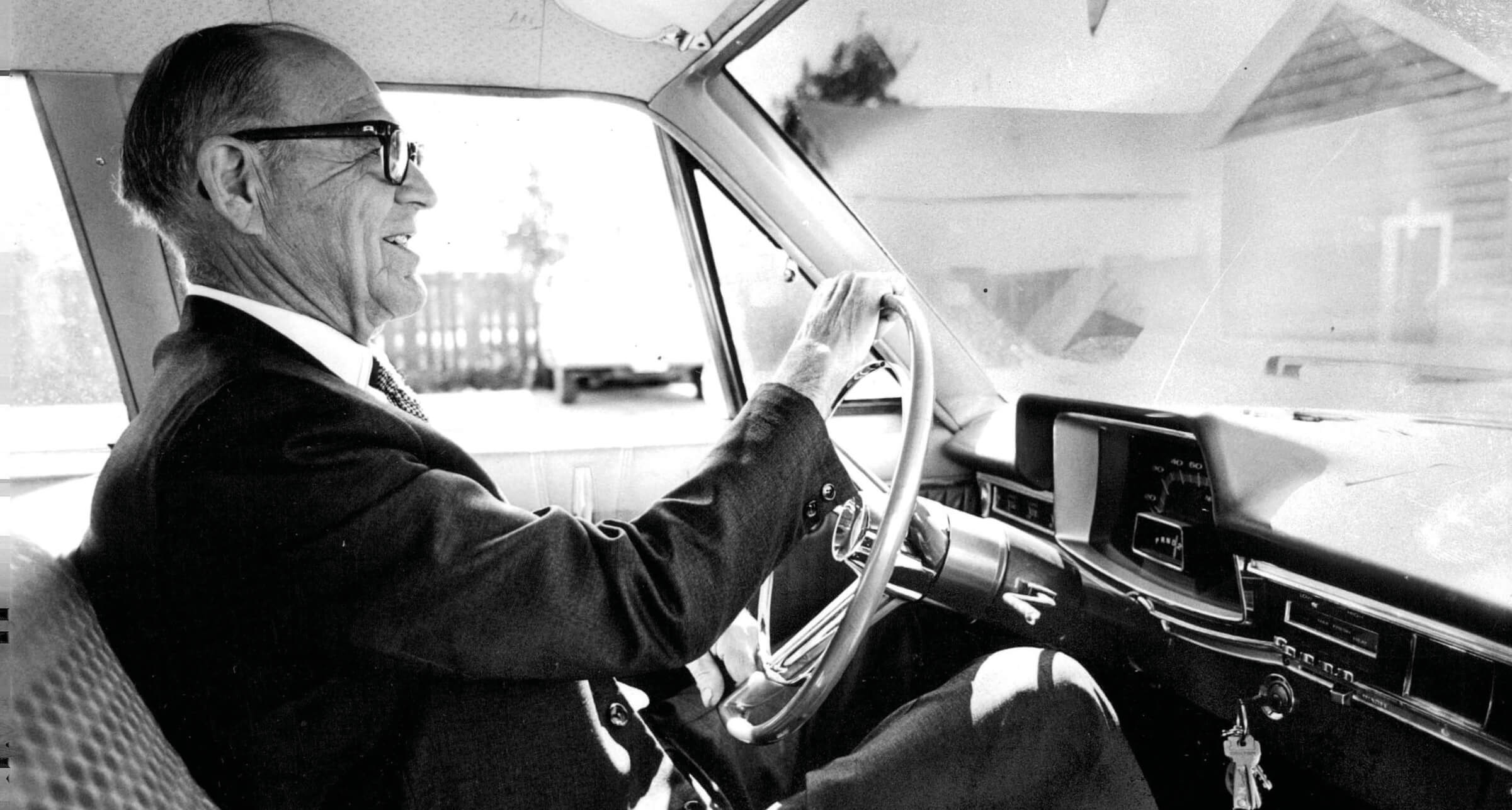 Vintage black and white photo of an older man driving an automobile