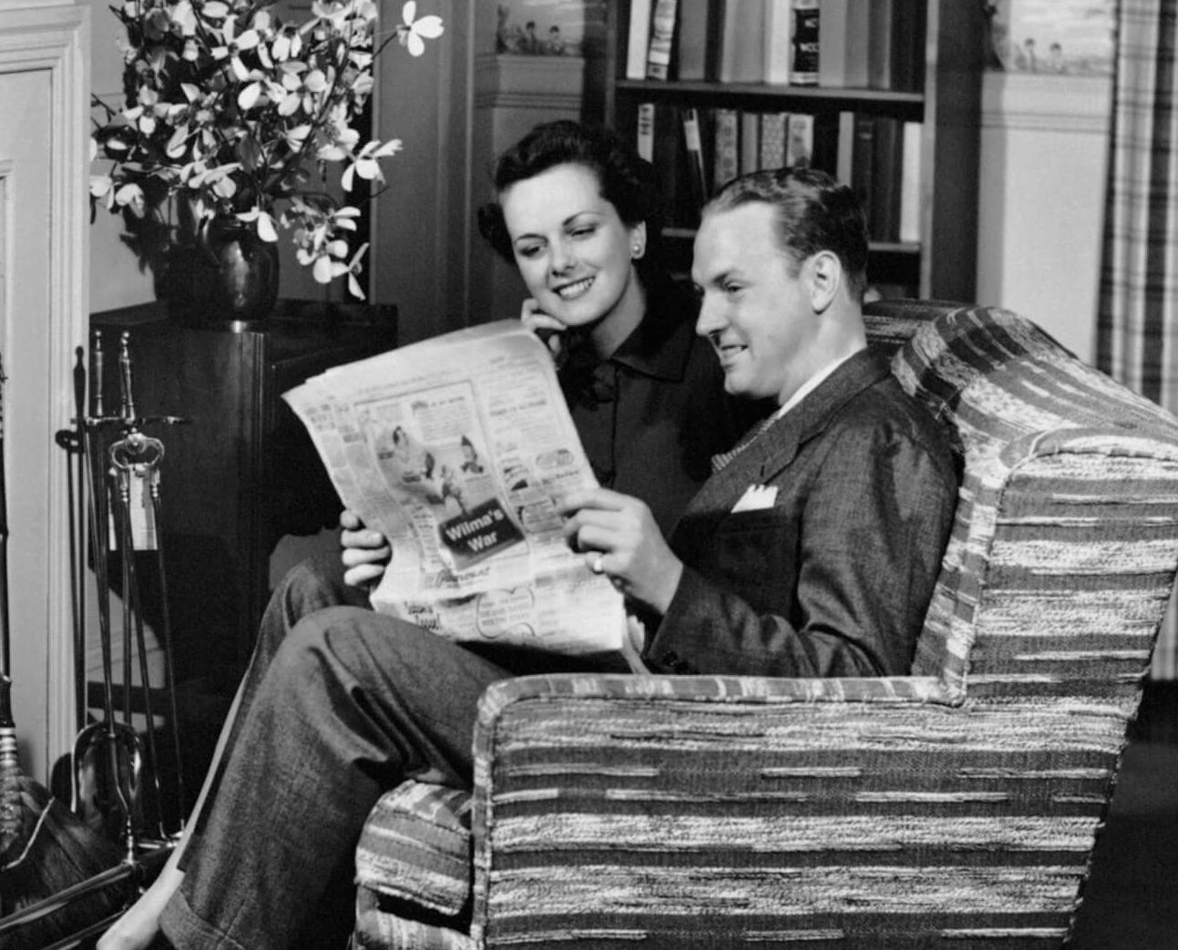 Vintage black and white photo of a couple sitting on a sofa reading a newspaper together