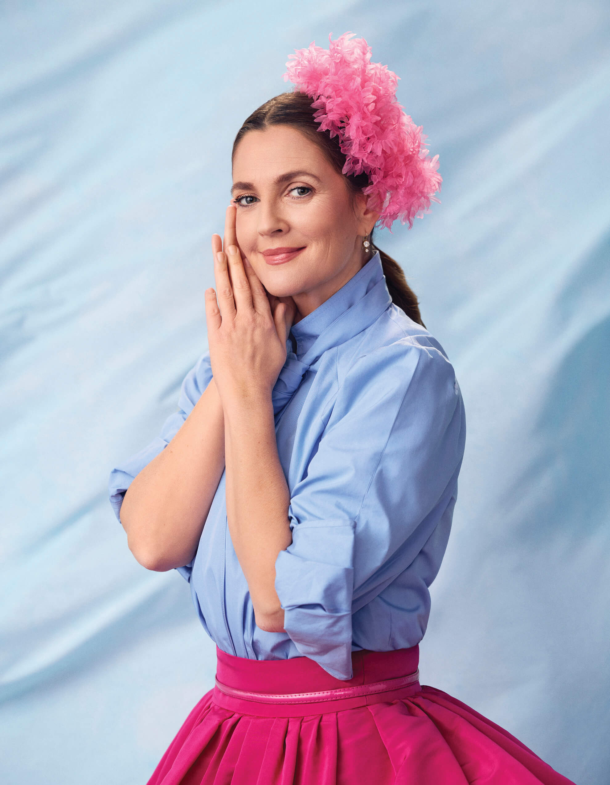 Photo of Drew Barrymore in a blue shirt and pink skirt, with a pink feather headpiece
