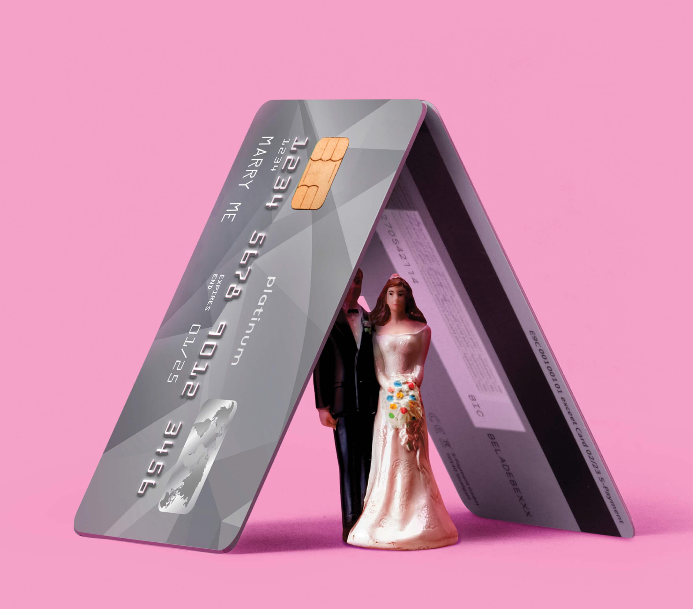 Photo illustration of two credit cards leaning on each other, underneath is a bride and groom cake topper